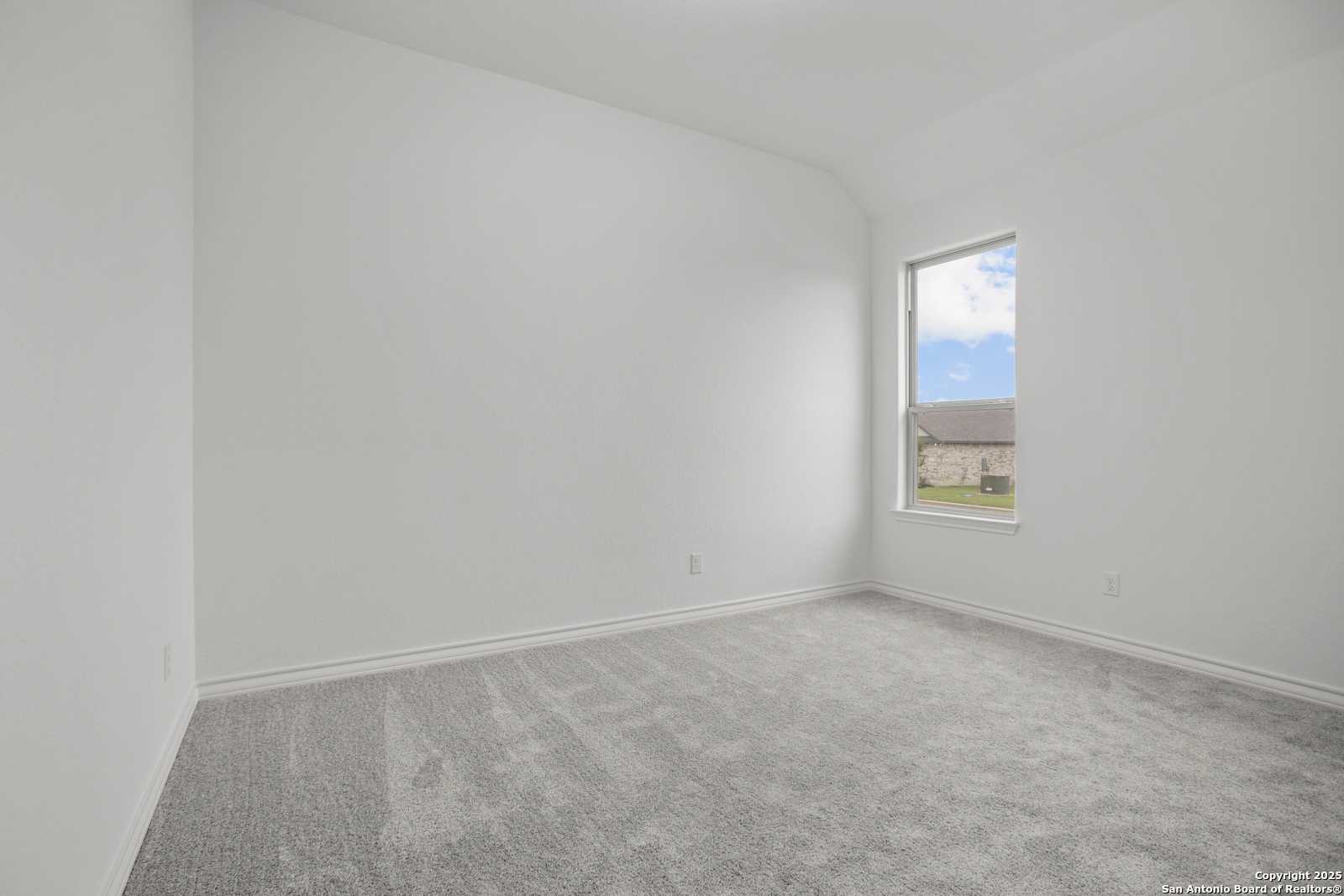 Spacious empty bedroom with white walls, gray carpet, sloped ceiling, and large window in Davidson Homes The Summerlin B, Castroville, Texas
