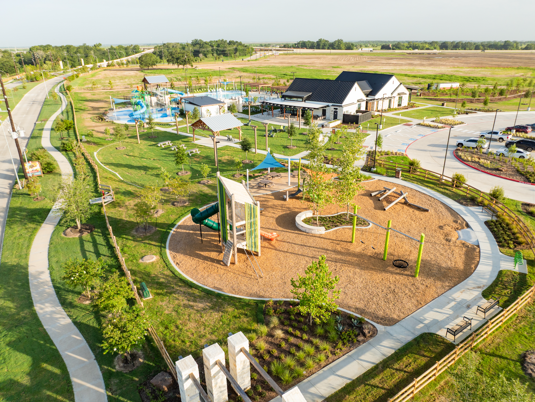 Vibrant playground with slides, climbers and splash pad at Emberly in Beasley Texas by Davidson Homes, surrounded by green lawns and pavilions