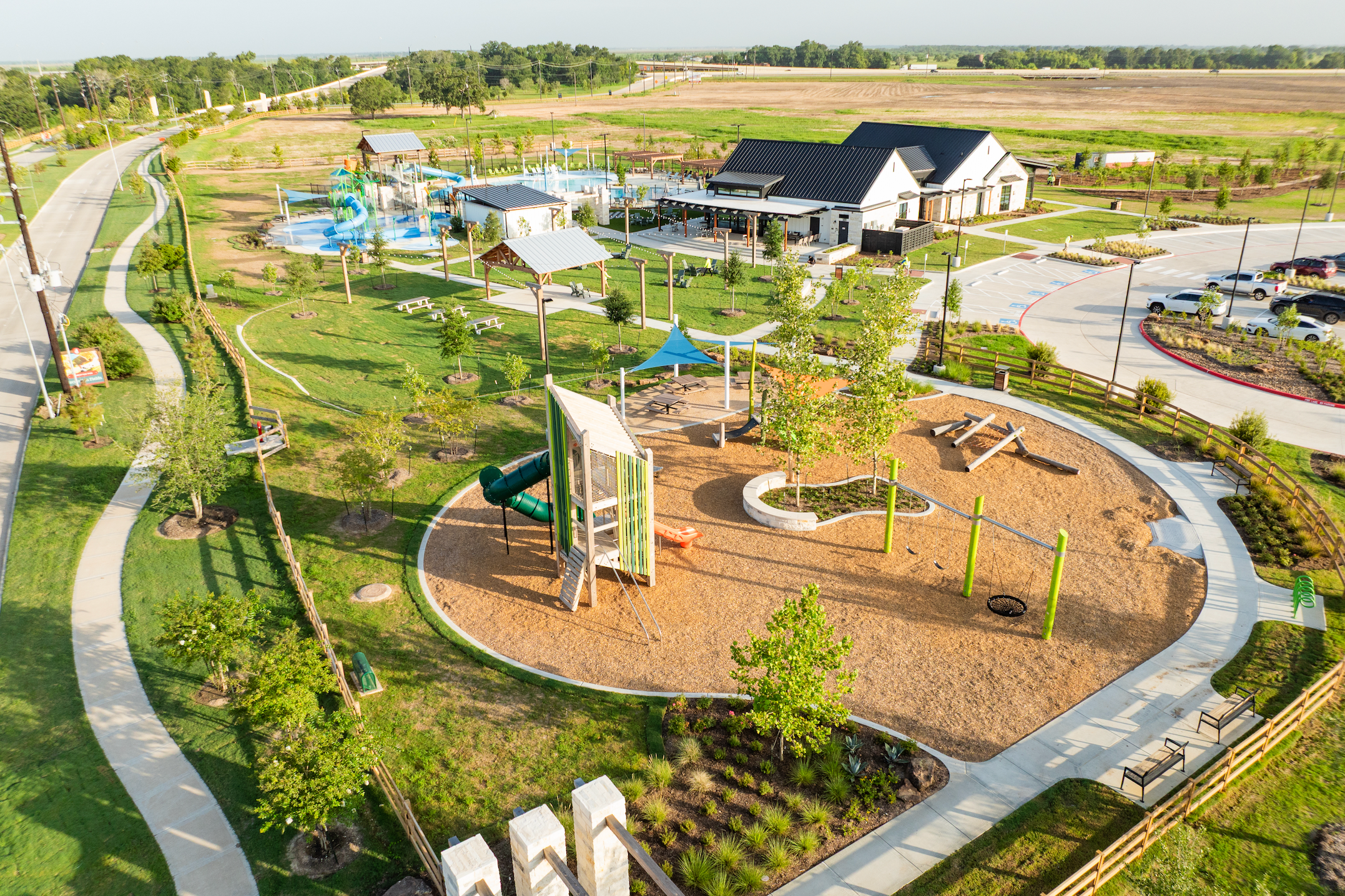 Vibrant playground with slides, climbers and splash pad at Emberly in Beasley Texas by Davidson Homes, surrounded by green lawns and pavilions