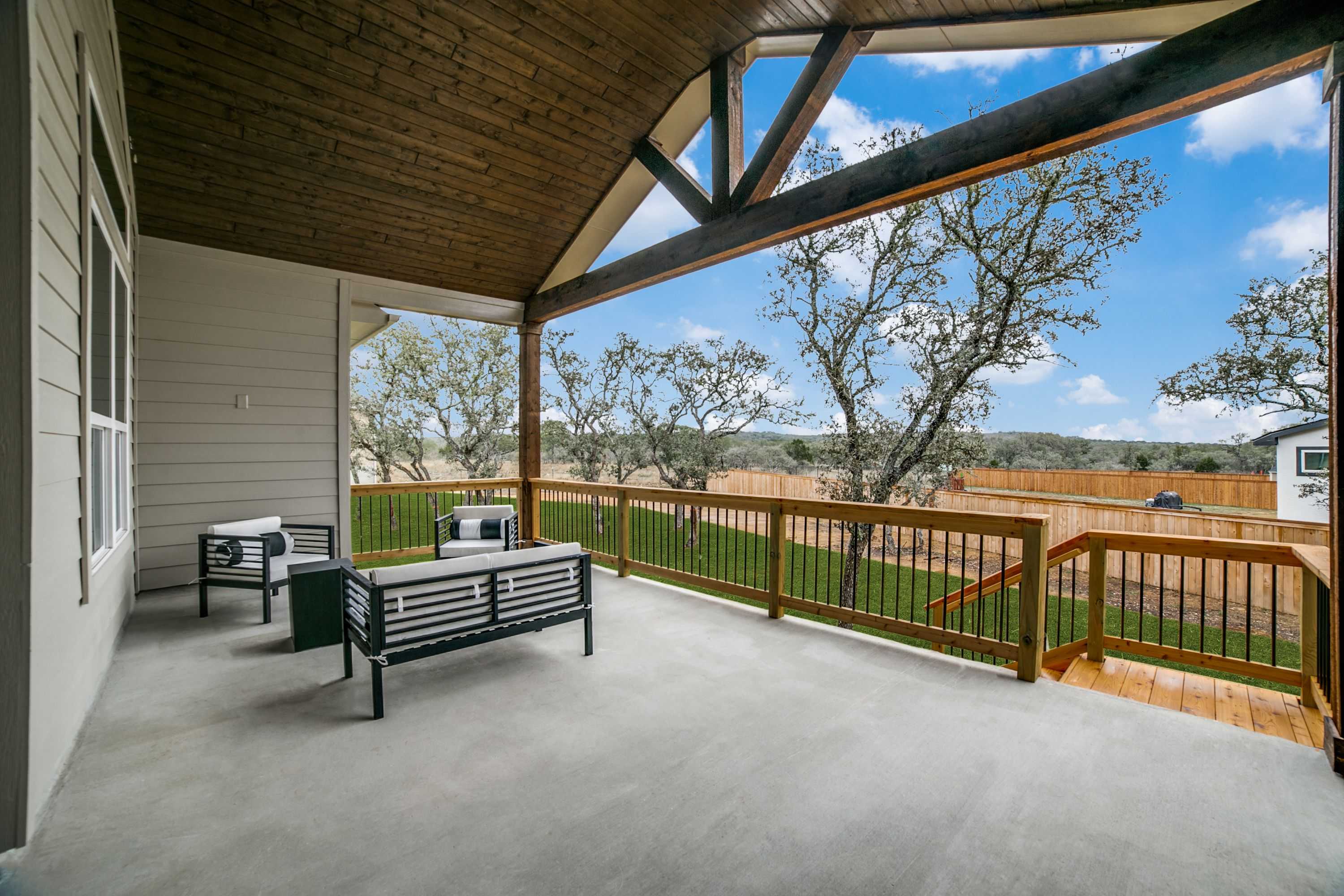 Spacious covered patio in The Garner A with vaulted wooden ceiling, black outdoor seating, wooden fence, and lush backyard view