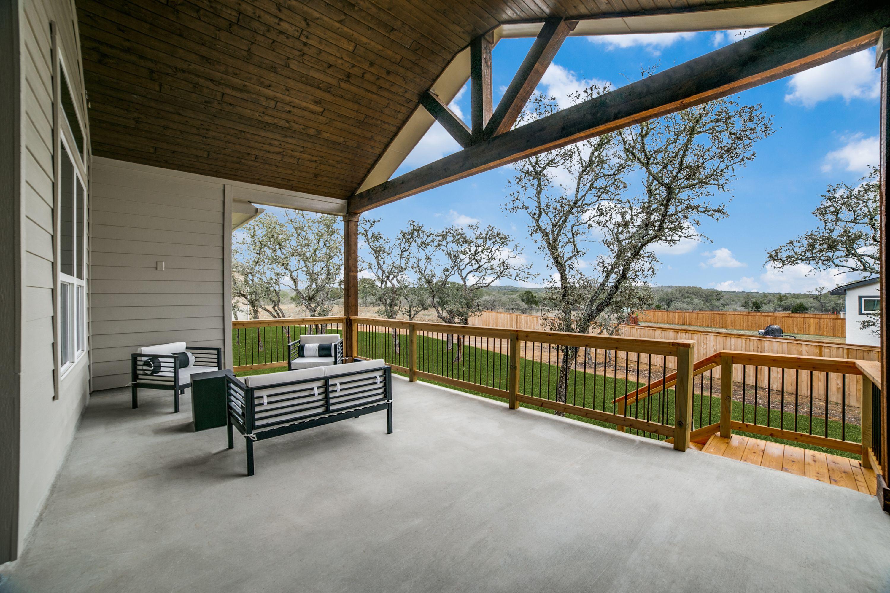Spacious covered patio in The Garner A with vaulted wooden ceiling, black outdoor seating, wooden fence, and lush backyard view