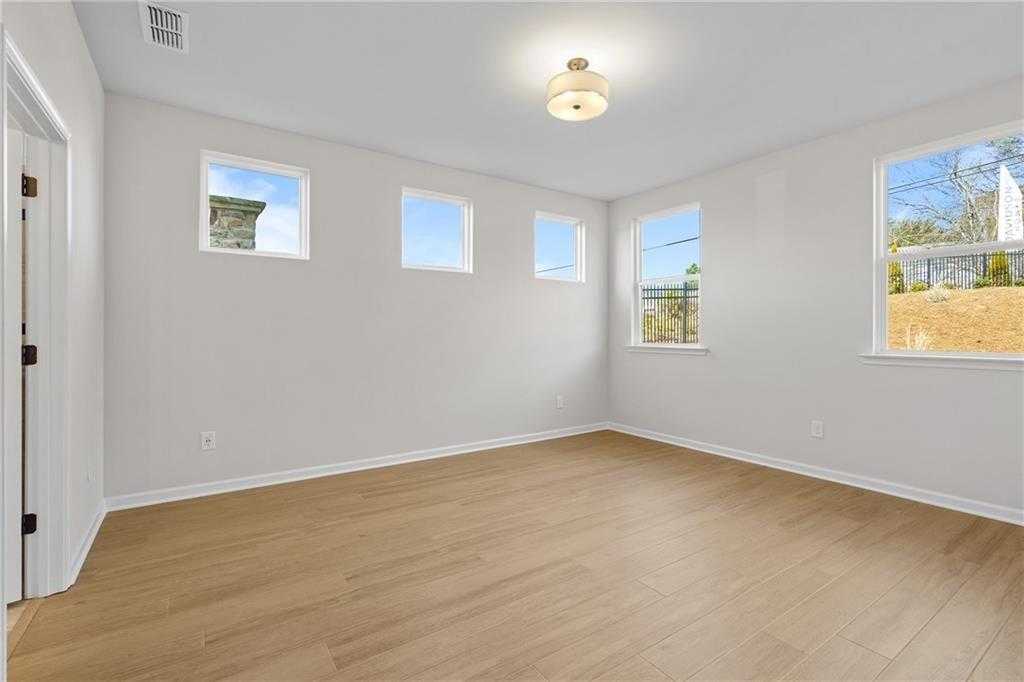 Bright bedroom with light gray walls, hardwood floors, and large windows in Davidson Homes The Edison A, Loganville, GA