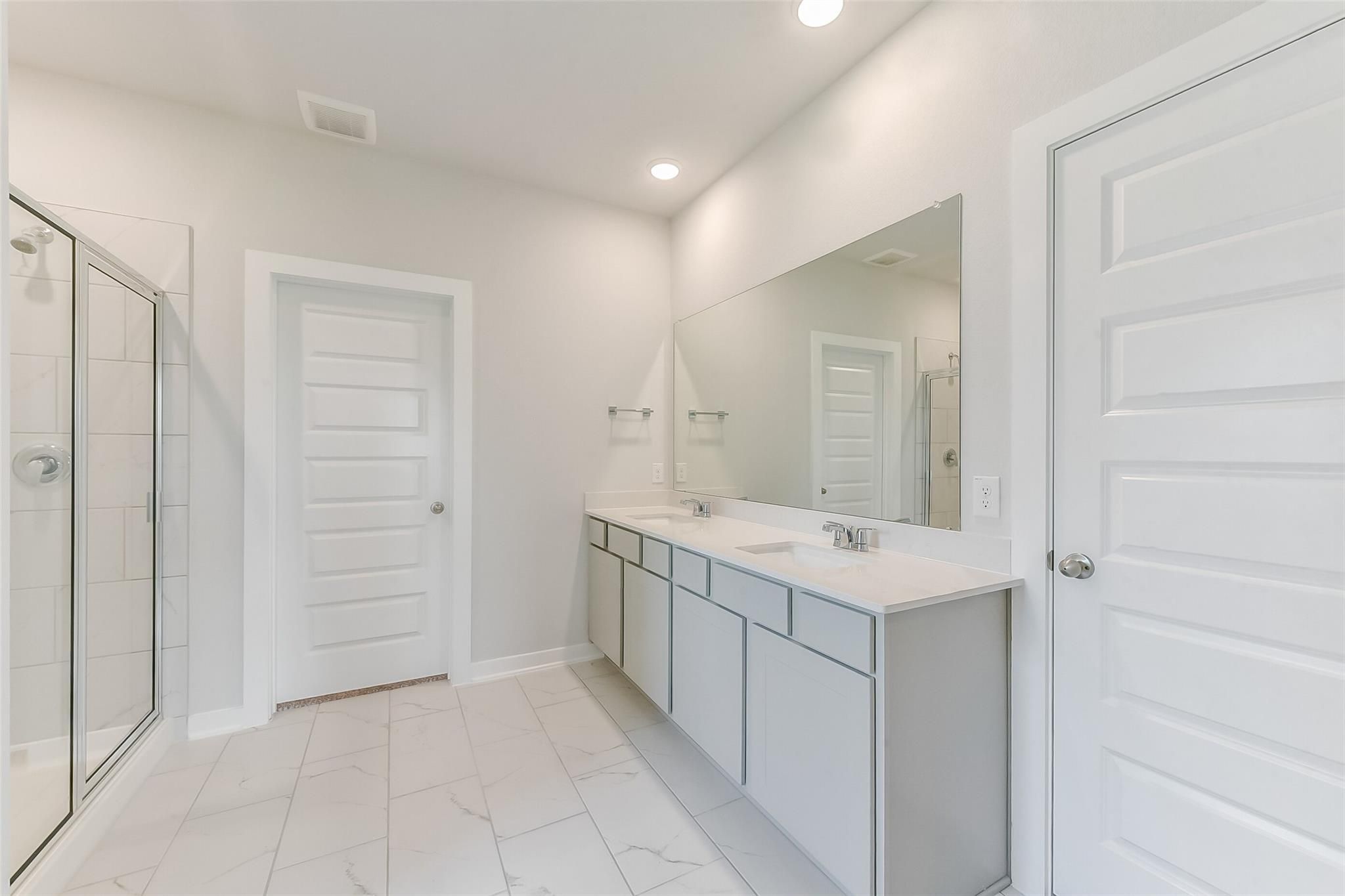 Modern master bathroom with double vanity, frameless glass shower, subway tile, and marble-look flooring in Davidson Homes The Tierra C, Dayton, Texas