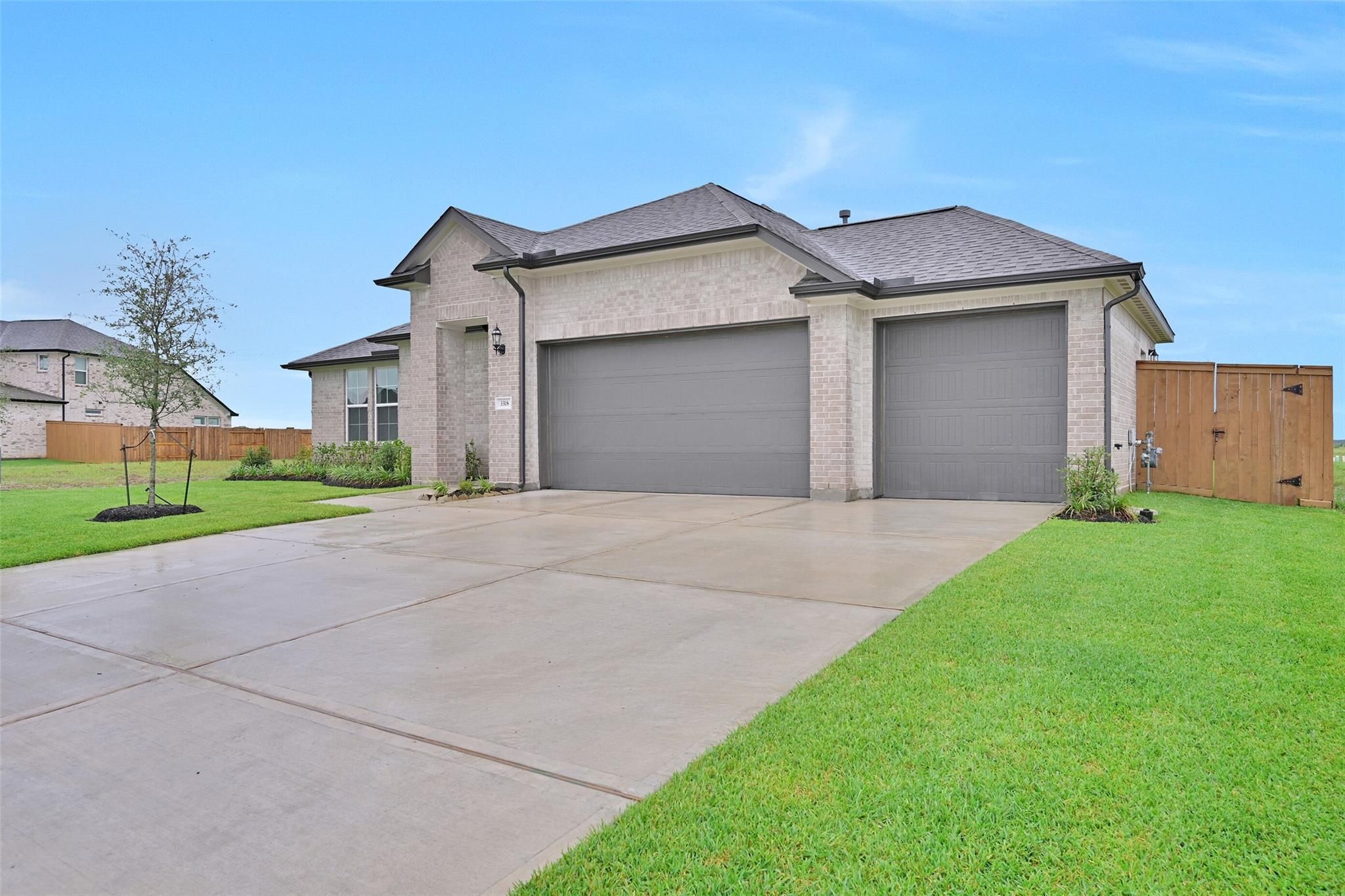 Modern beige brick single-story home with 3-car garage, concrete driveway, and landscaped front yard in Lago Mar, Texas City