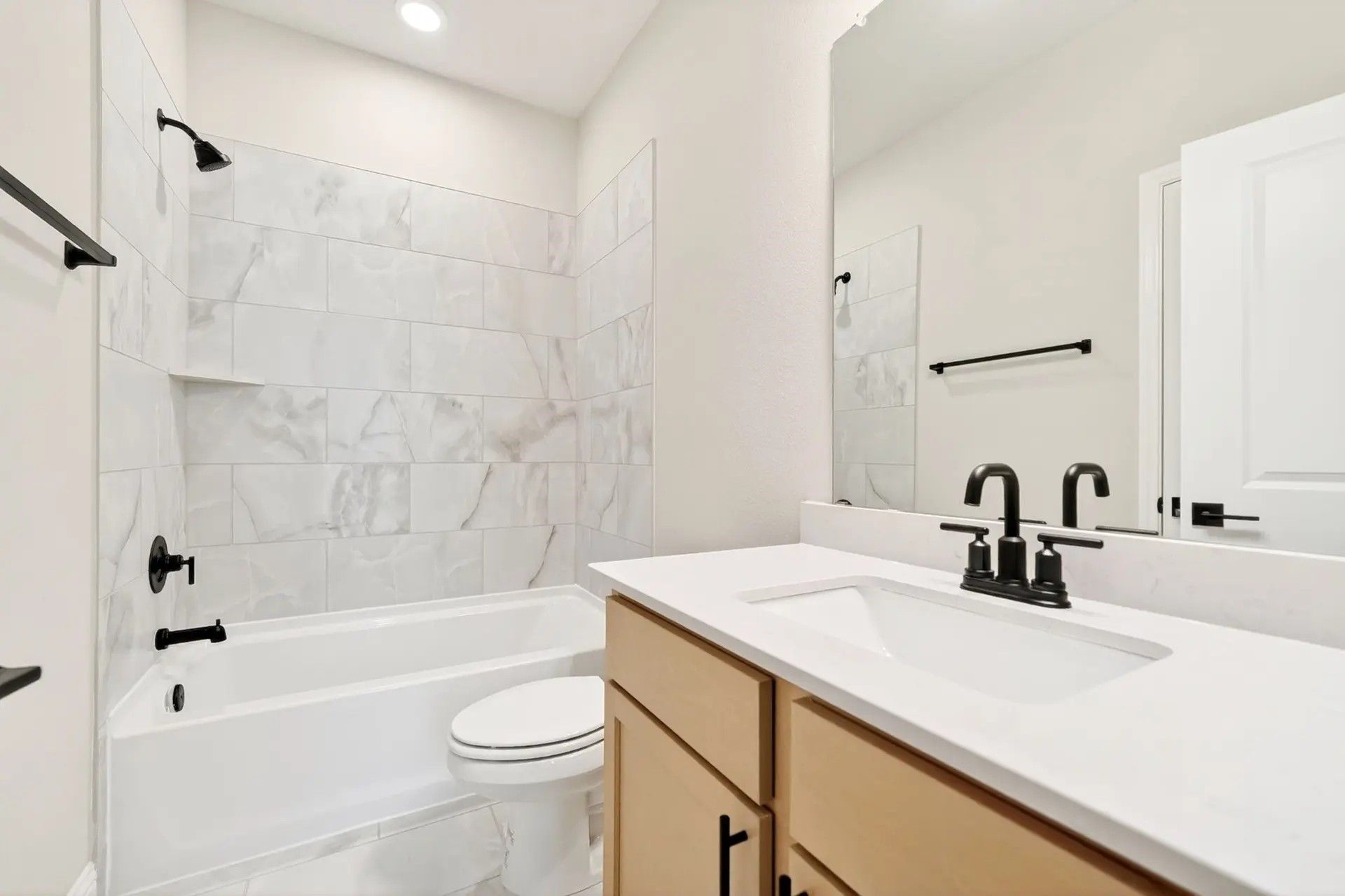 Modern bathroom with marble-style tile shower, light wood vanity, and black fixtures in Davidson Homes' The Holly C floor plan.