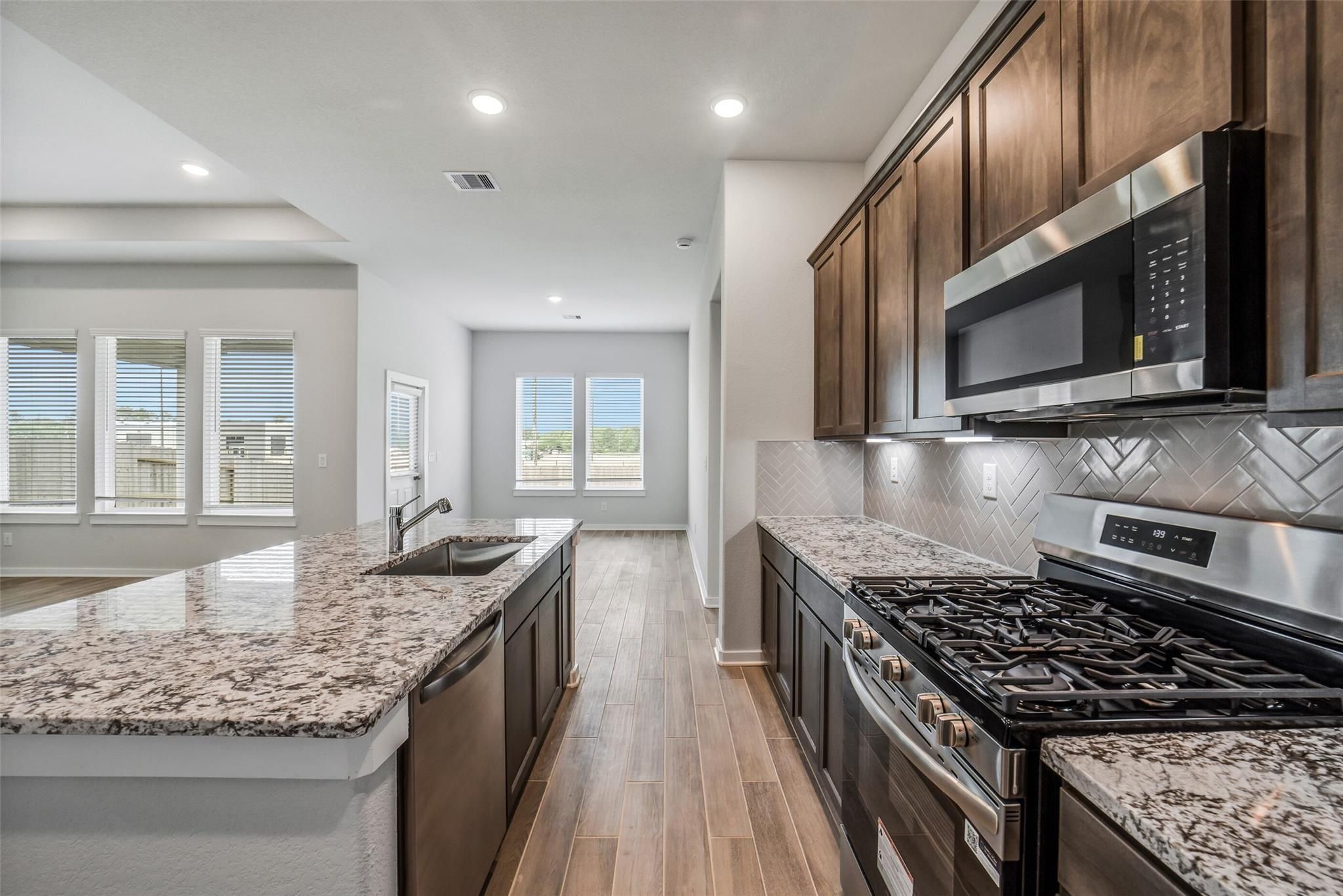 Open-concept kitchen with granite countertops, shaker cabinets, stainless appliances and herringbone backsplash in The Acadia C, Magnolia TX