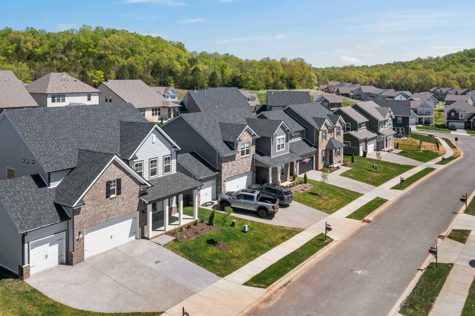Modern homes with dark shingle roofs and garages lining street at Carellton in Gallatin Tennessee amid green hills