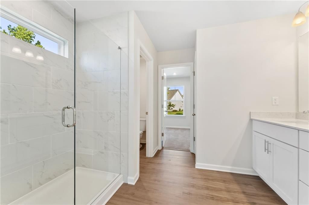 Modern master bathroom with frameless glass shower, subway tile walls, and oak wood floors in Davidson Homes The Willow B, Riverwood, Dallas, GA