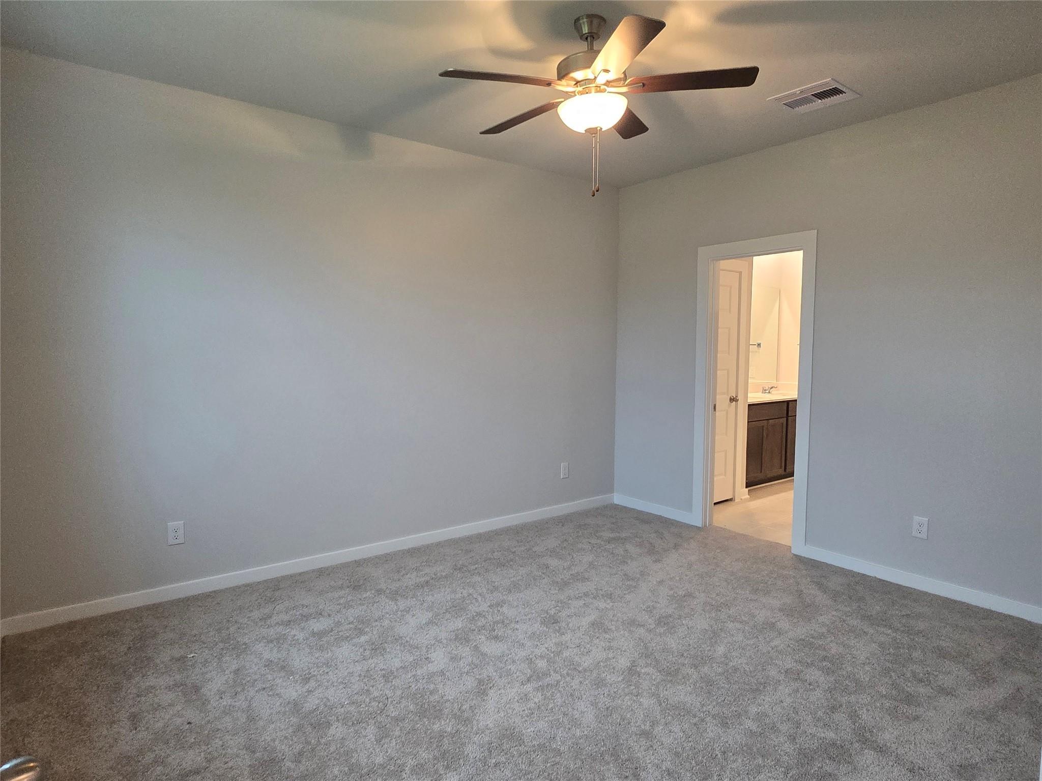 Spacious empty bedroom with ceiling fan, gray walls, beige carpet, and en-suite bath with double vanity in Davidson Homes The Brazos E, Cleveland TX