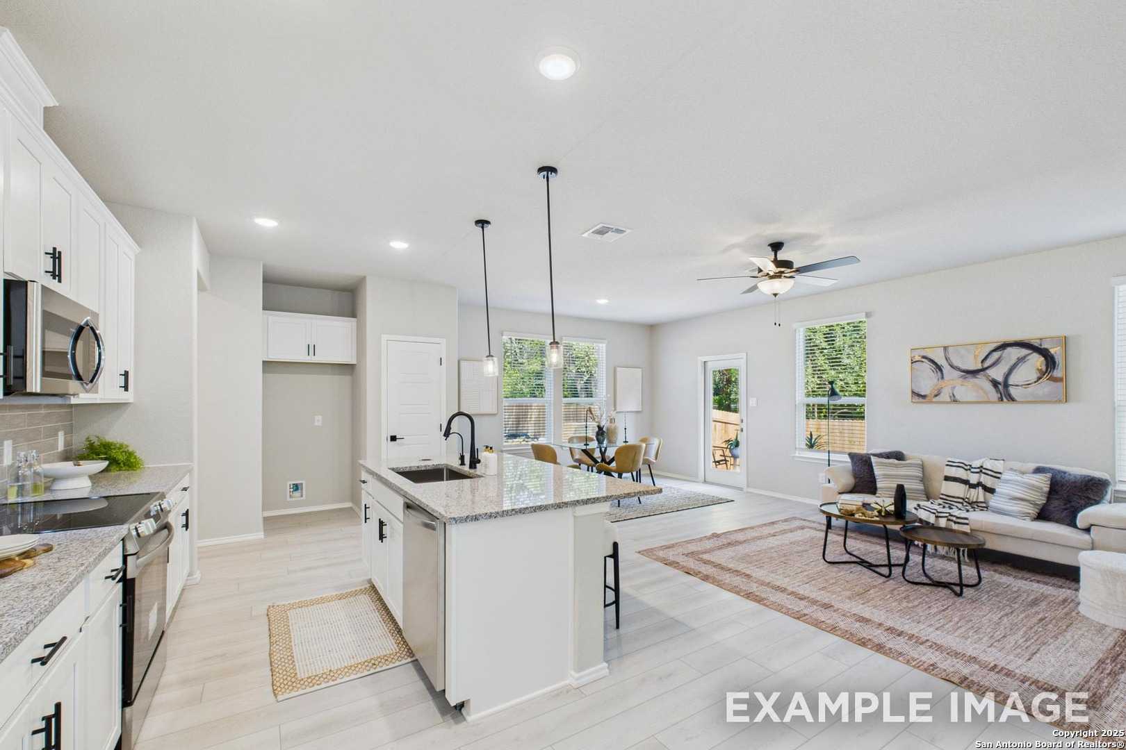 Open-concept kitchen with white cabinets, stainless appliances, large island, and living area in Davidson Homes The Charlotte A, San Antonio