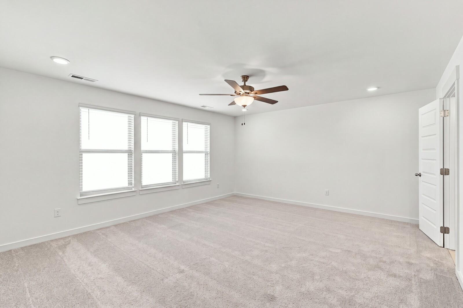 Spacious carpeted bedroom with ceiling fan and three windows in Davidson Homes The Willow C, Gallatin, Tennessee