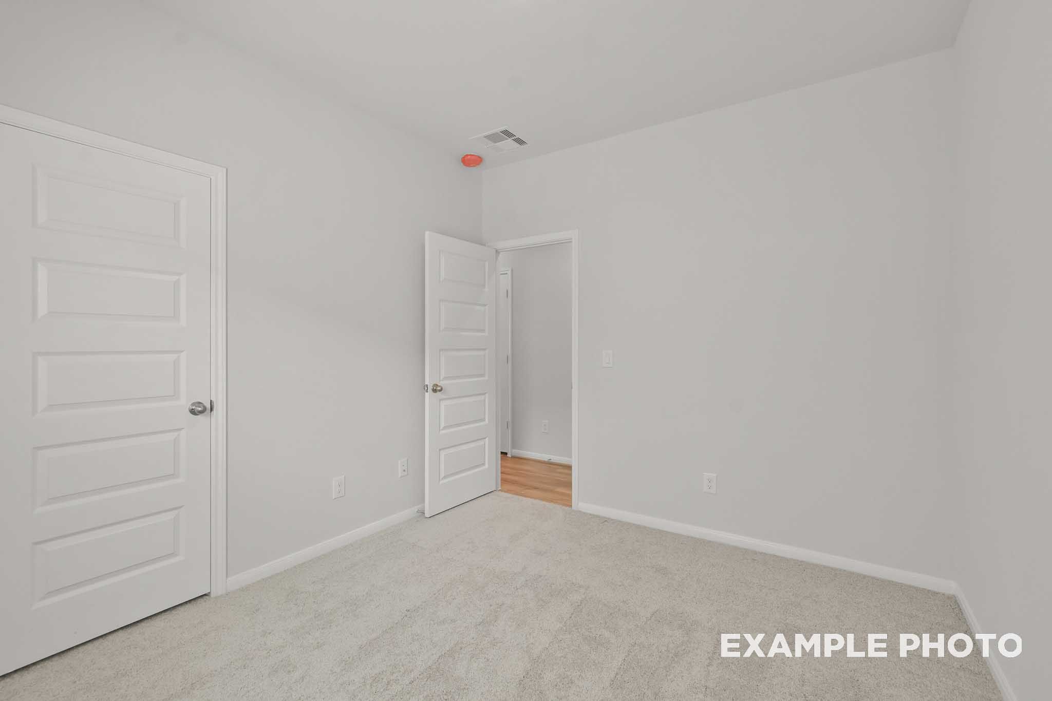 Spacious secondary bedroom in The Comal floor plan with white walls, beige carpet, closet door, and adjacent wood flooring
