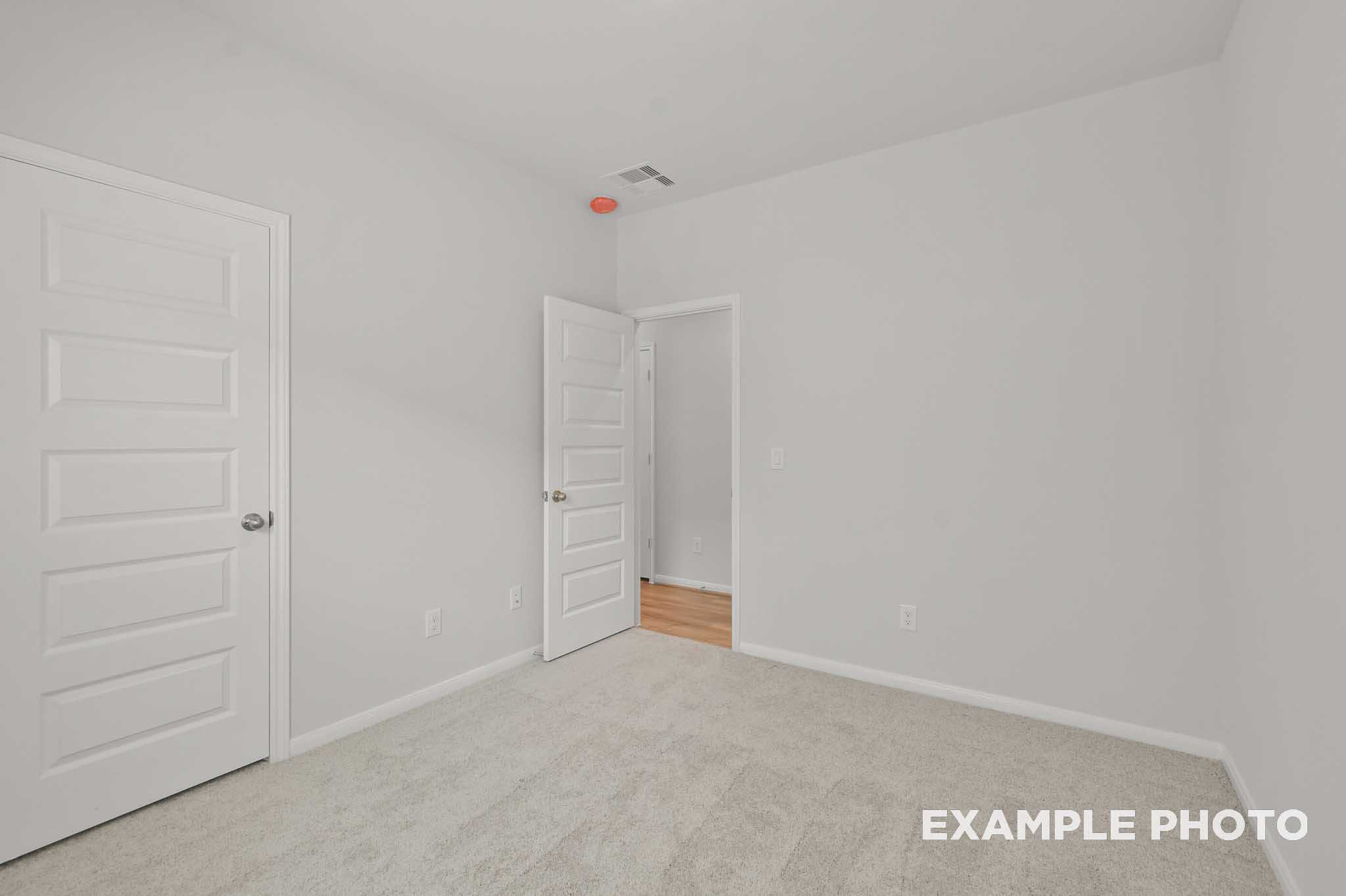 Spacious secondary bedroom in The Comal floor plan with white walls, beige carpet, closet door, and adjacent wood flooring