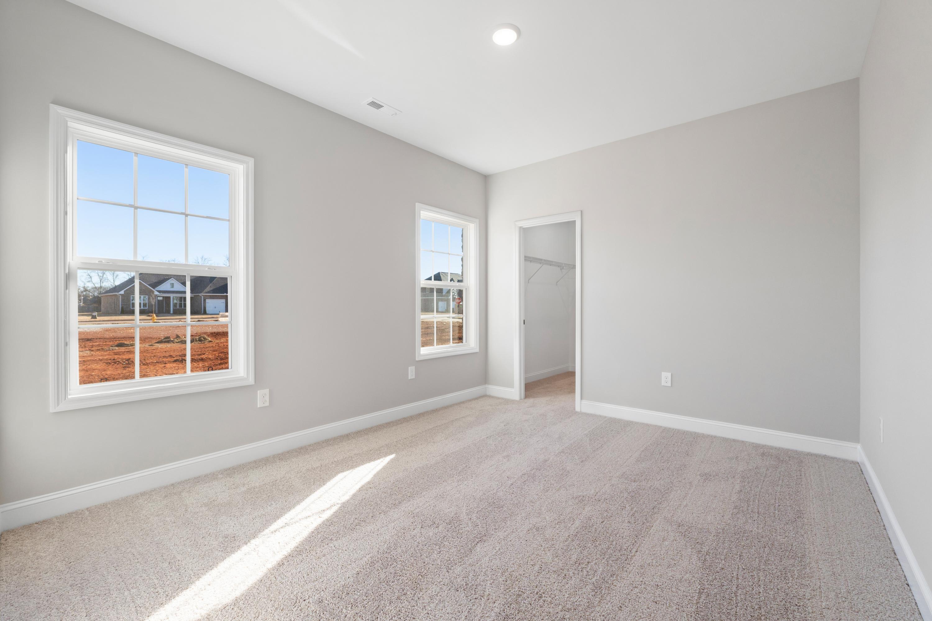Spacious master bedroom in The Valencia by Davidson Homes, Meridianville AL, featuring gray walls, beige carpet, large windows with construction view