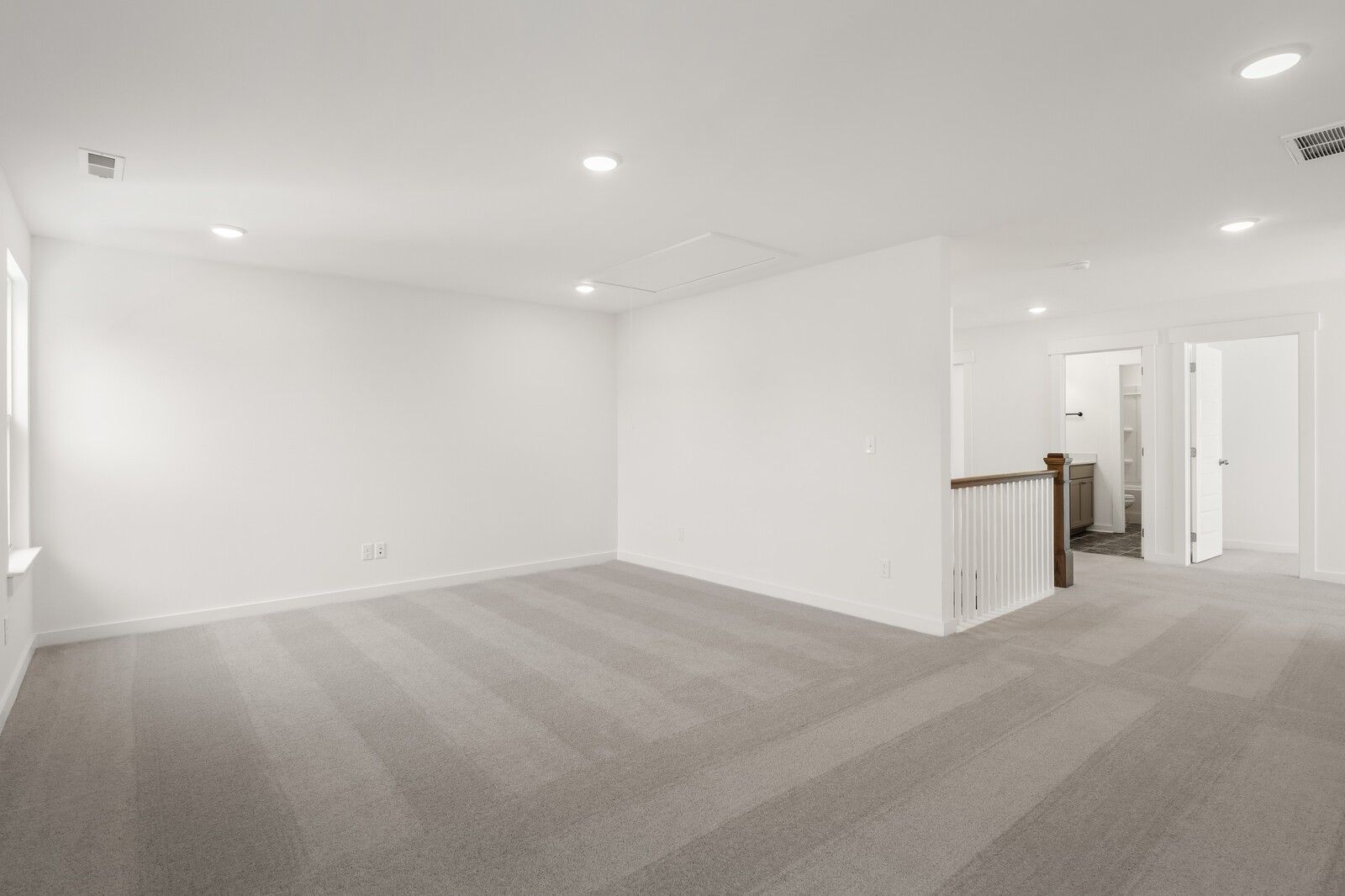 Spacious upstairs loft with white walls, gray carpet, and wooden staircase railing in The Ash A home, Gallatin, TN