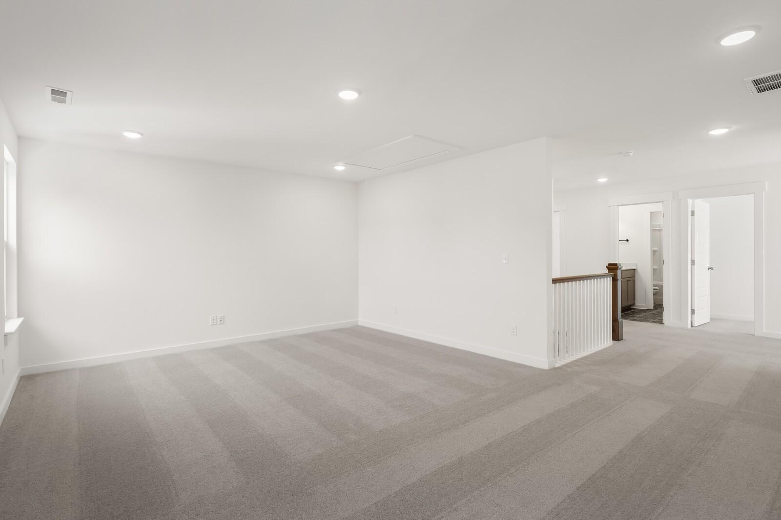 Spacious upstairs loft with white walls, gray carpet, and wooden staircase railing in The Ash A home, Gallatin, TN