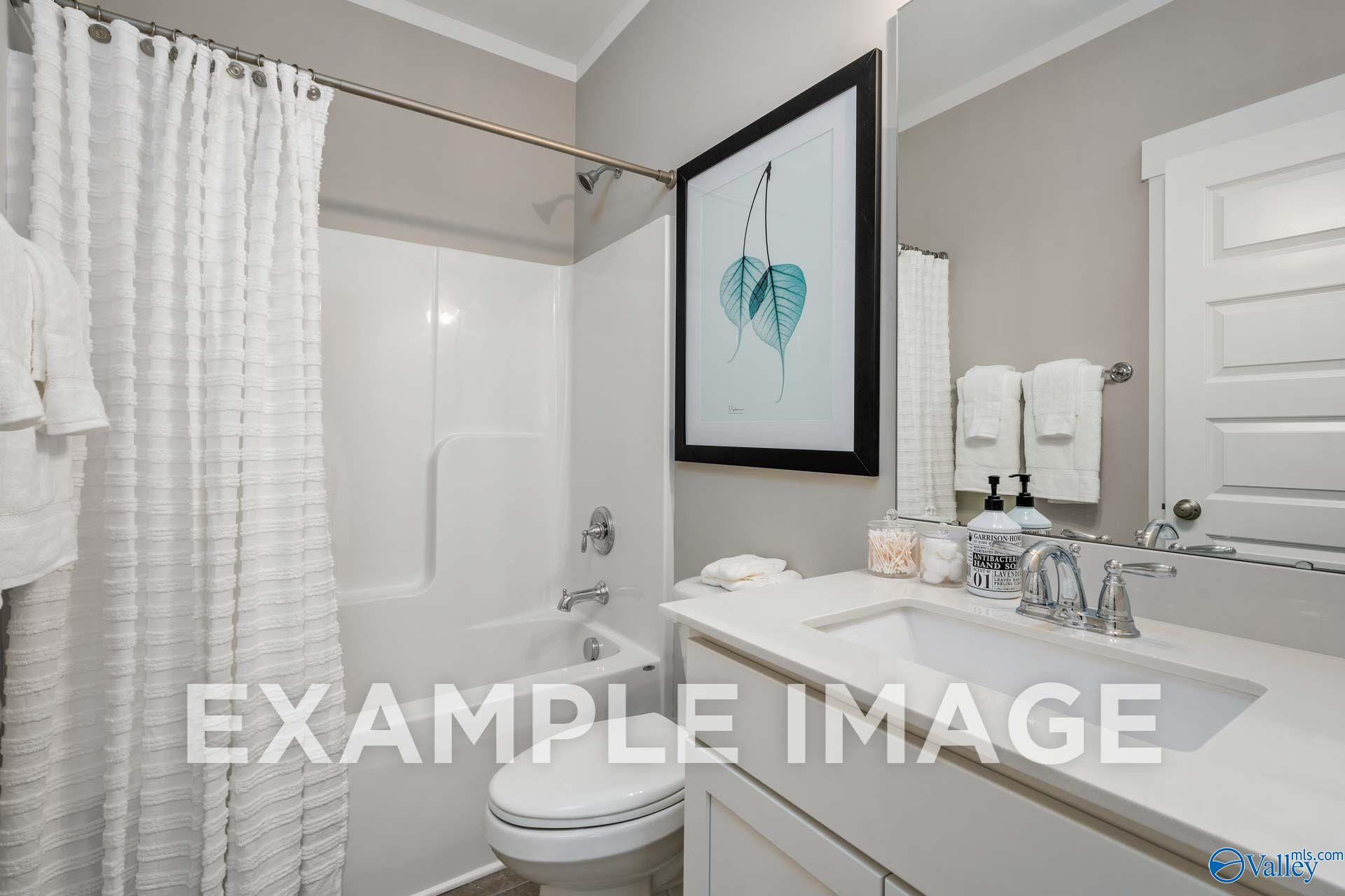 Bright white bathroom with tub, shower curtain, and vanity sink in Davidson Homes The Harrison floor plan, Hartselle, Alabama