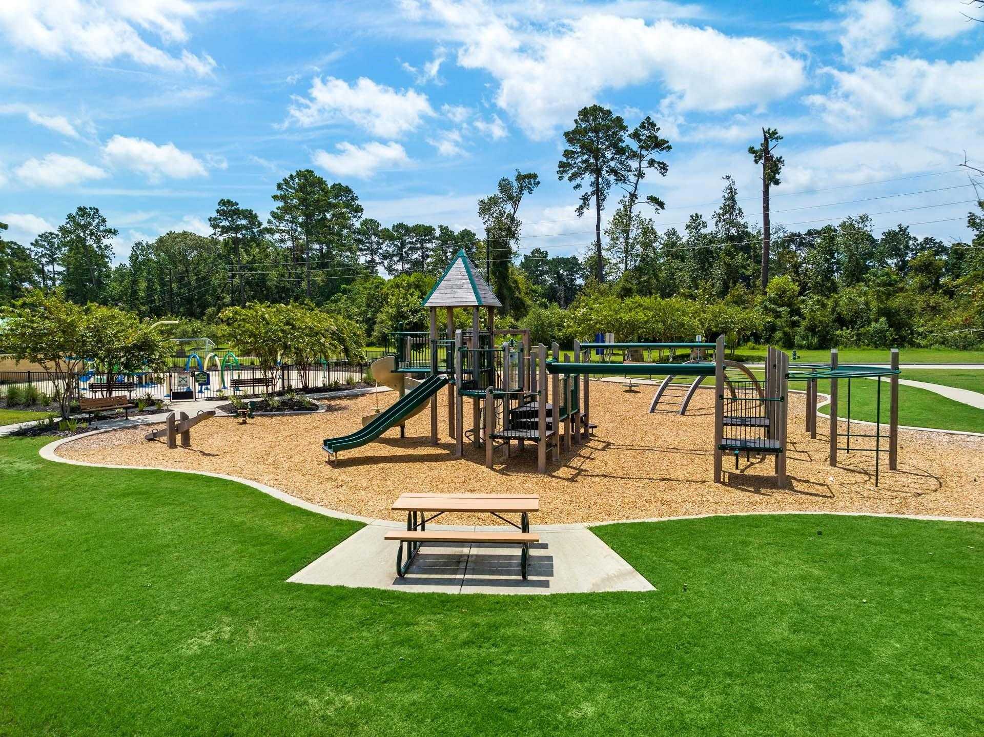 Vibrant community playground with slides, swings, climbing towers, picnic table amid lush trees in Lakes at Black Oak, Magnolia, Texas