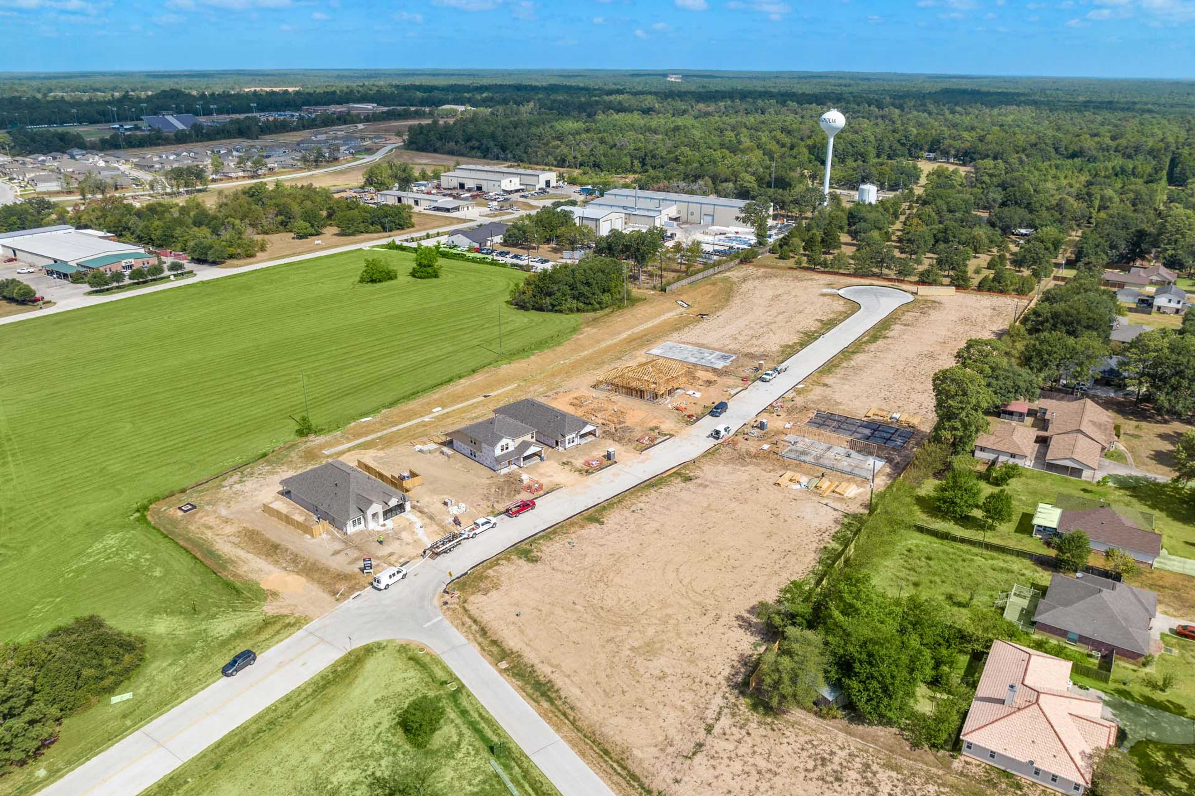 Aerial view of new home construction at Windmill Estates in Magnolia Texas with green fields, wooded areas, and water tower