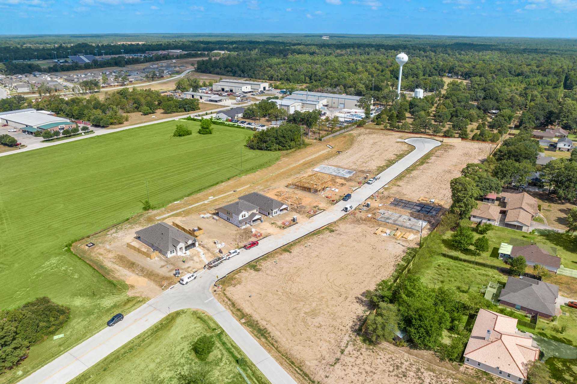 Aerial view of new home construction at Windmill Estates in Magnolia Texas featuring building sites green fields woods and water tower