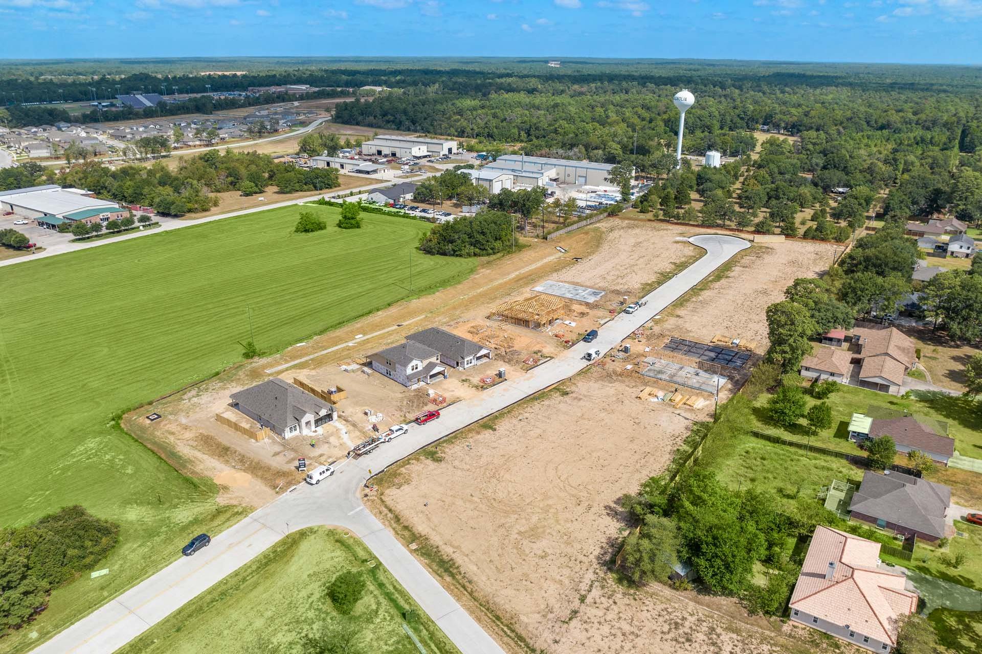 Aerial view of new home construction at Windmill Estates in Magnolia Texas featuring building sites green fields woods and water tower