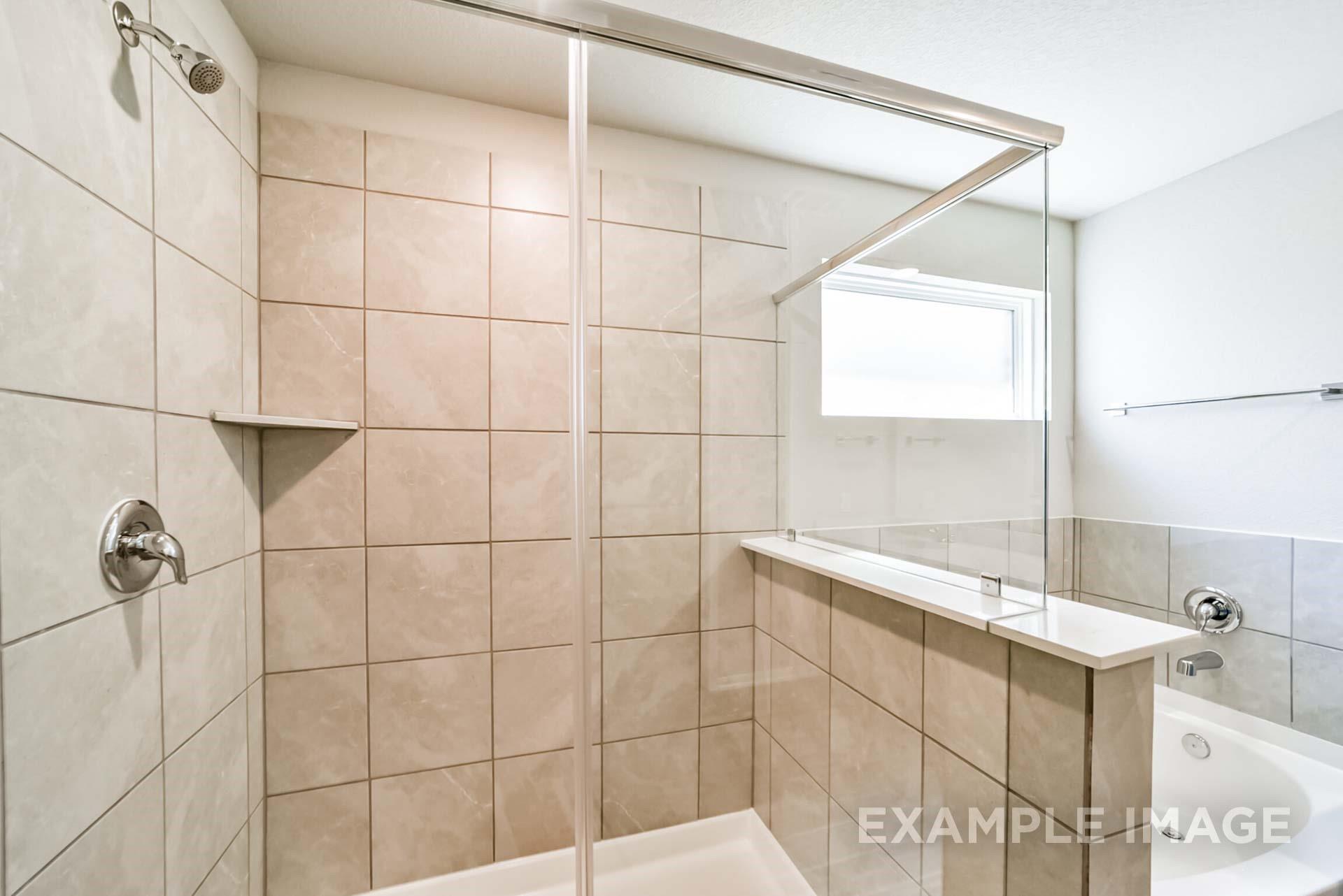 Tiled walk-in shower with glass enclosure in The Riviera A floor plan at Emberly in Beasley, Texas.