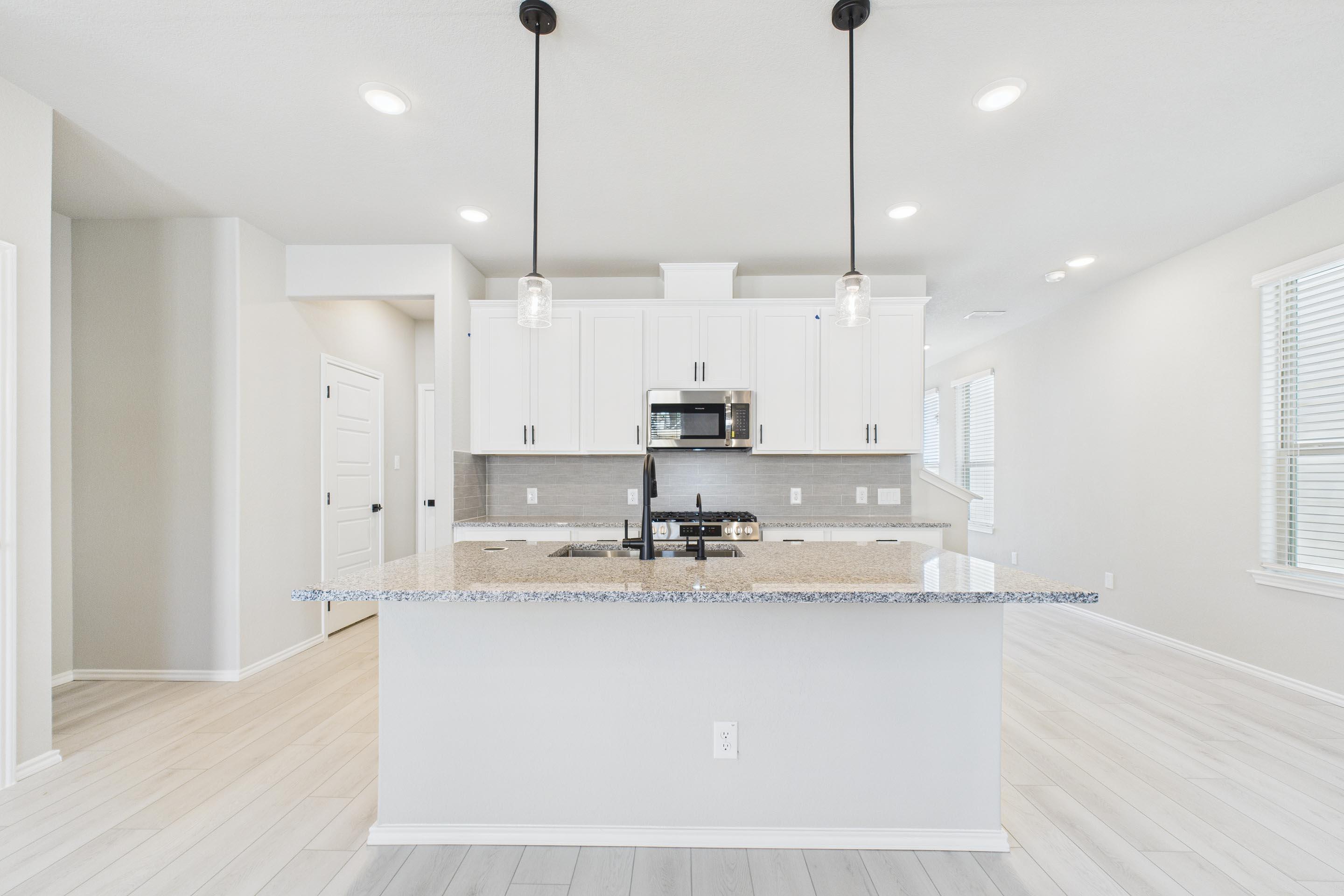 Modern kitchen in The Charlotte A featuring white cabinets, granite island, and pendant lighting in a San Antonio home.