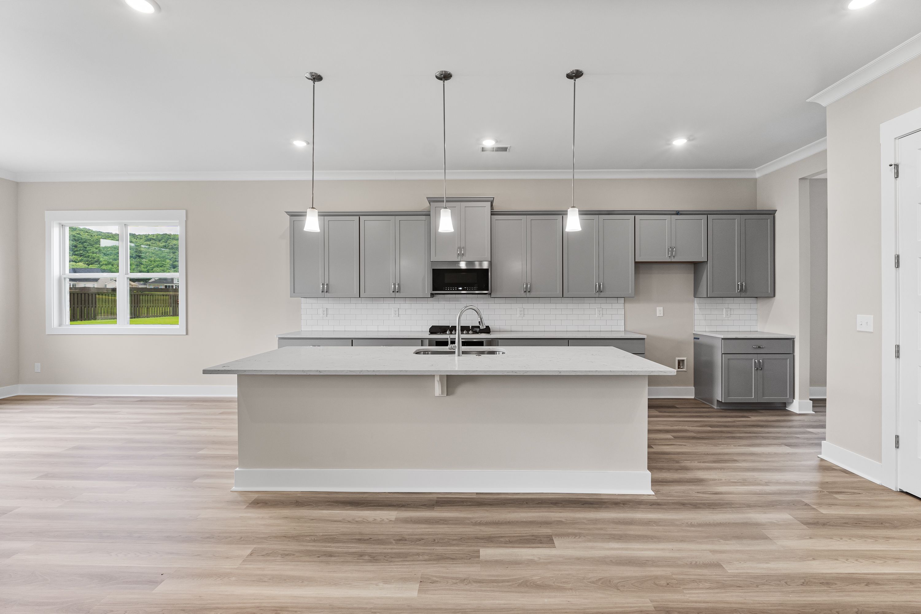 Modern kitchen in The Oxford A home design featuring large white island, gray shaker cabinets, and pendant lights
