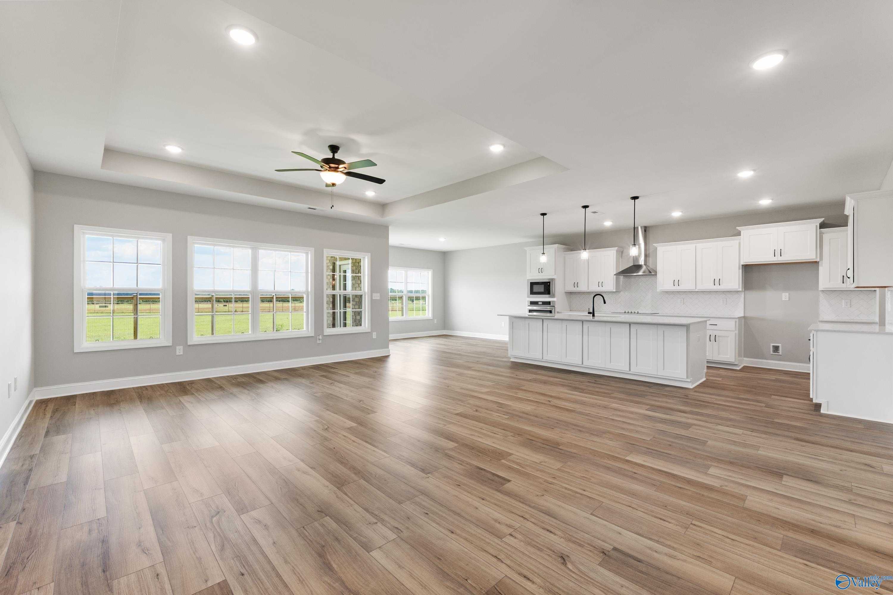Open kitchen with white cabinets, island sink, ceiling fan, and large windows overlooking fields in Davidson Homes Rockford B, Toney, AL