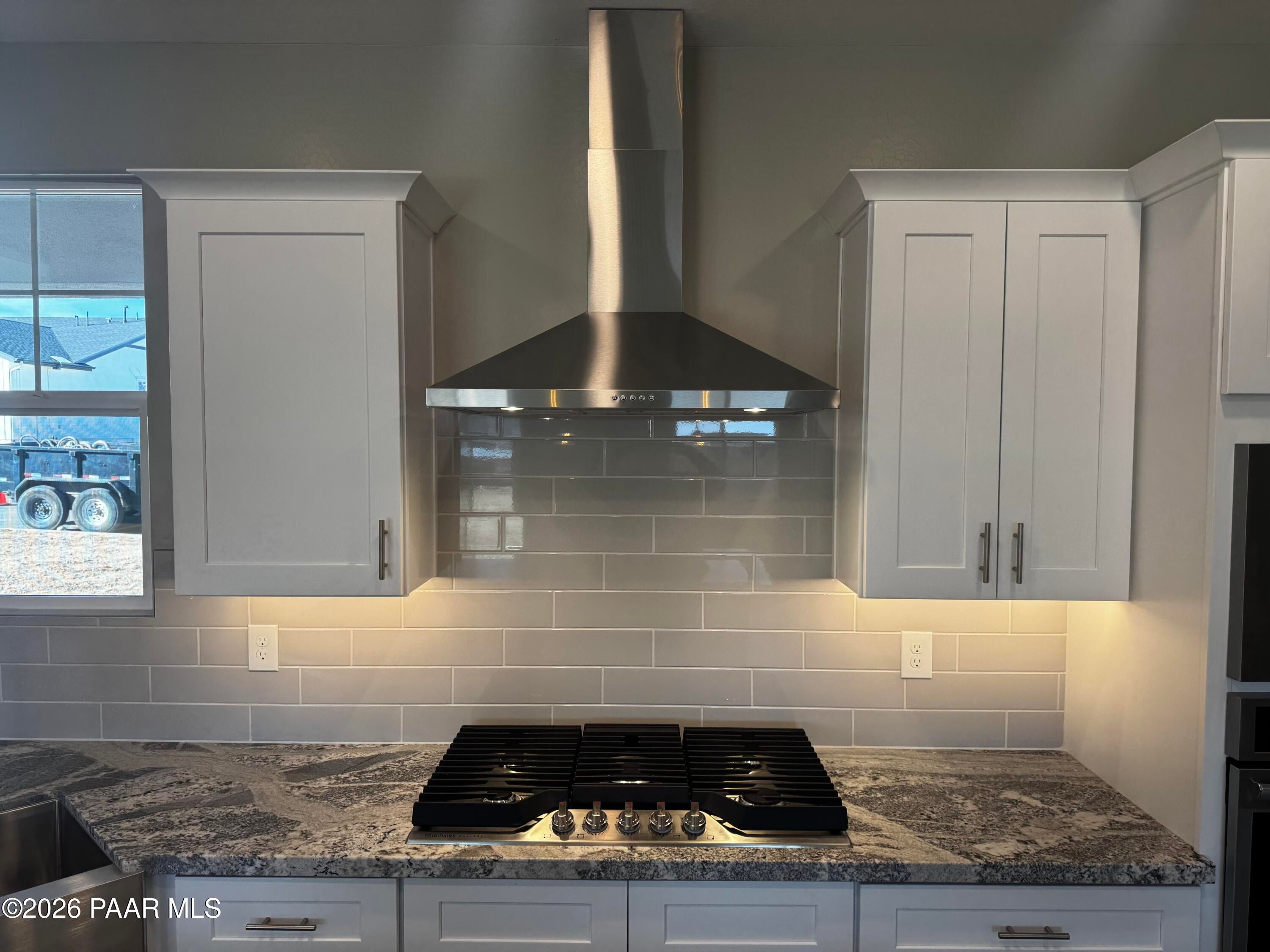 Modern kitchen with white shaker cabinets, stainless steel hood over gas range, granite counters, subway tile backsplash in Davidson Homes Daybreak B, Prescott AZ