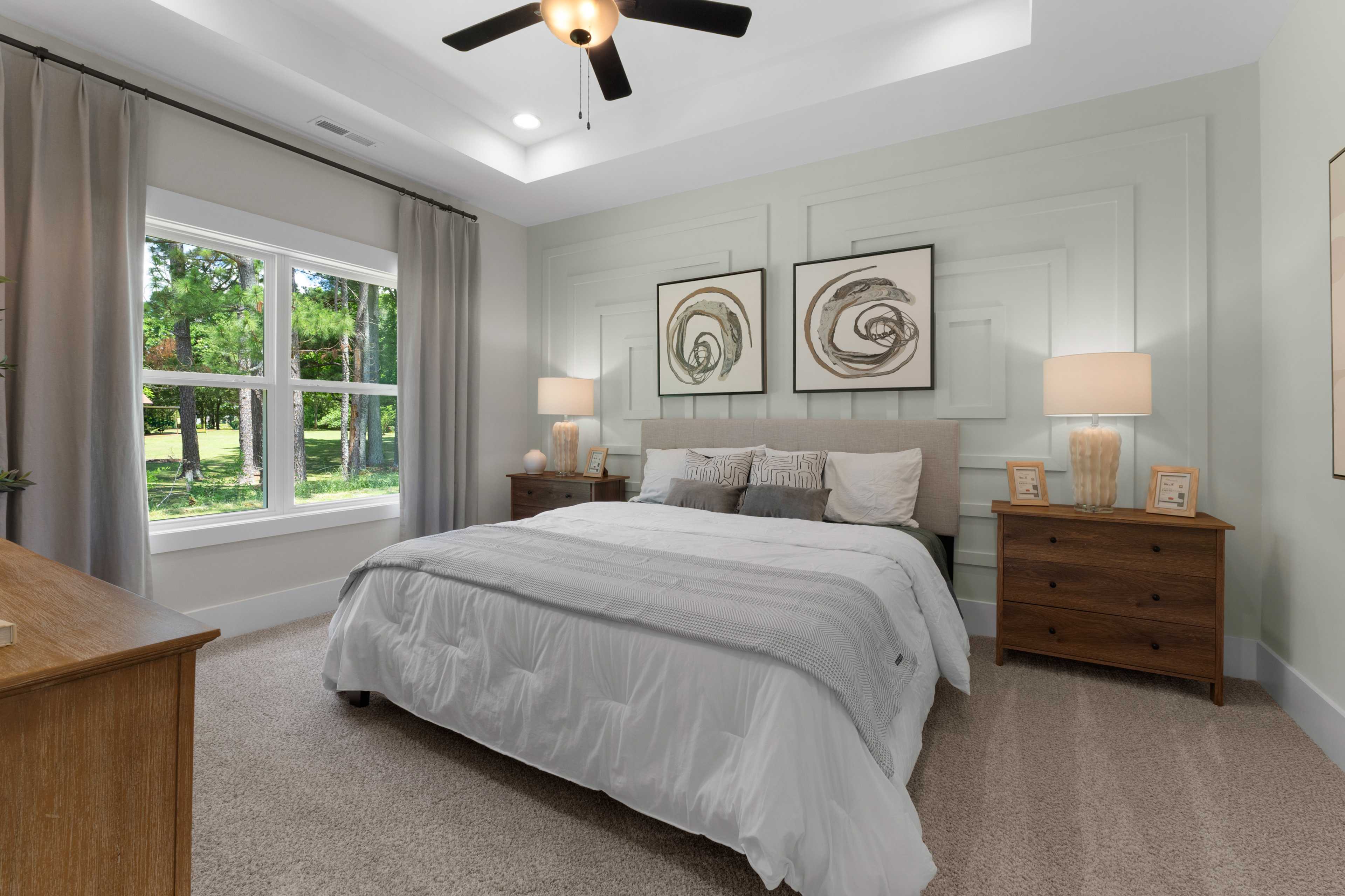 Spacious primary bedroom at Hollon Meadow in Decatur Alabama with king bed, neutral walls, abstract art, and tree-view windows