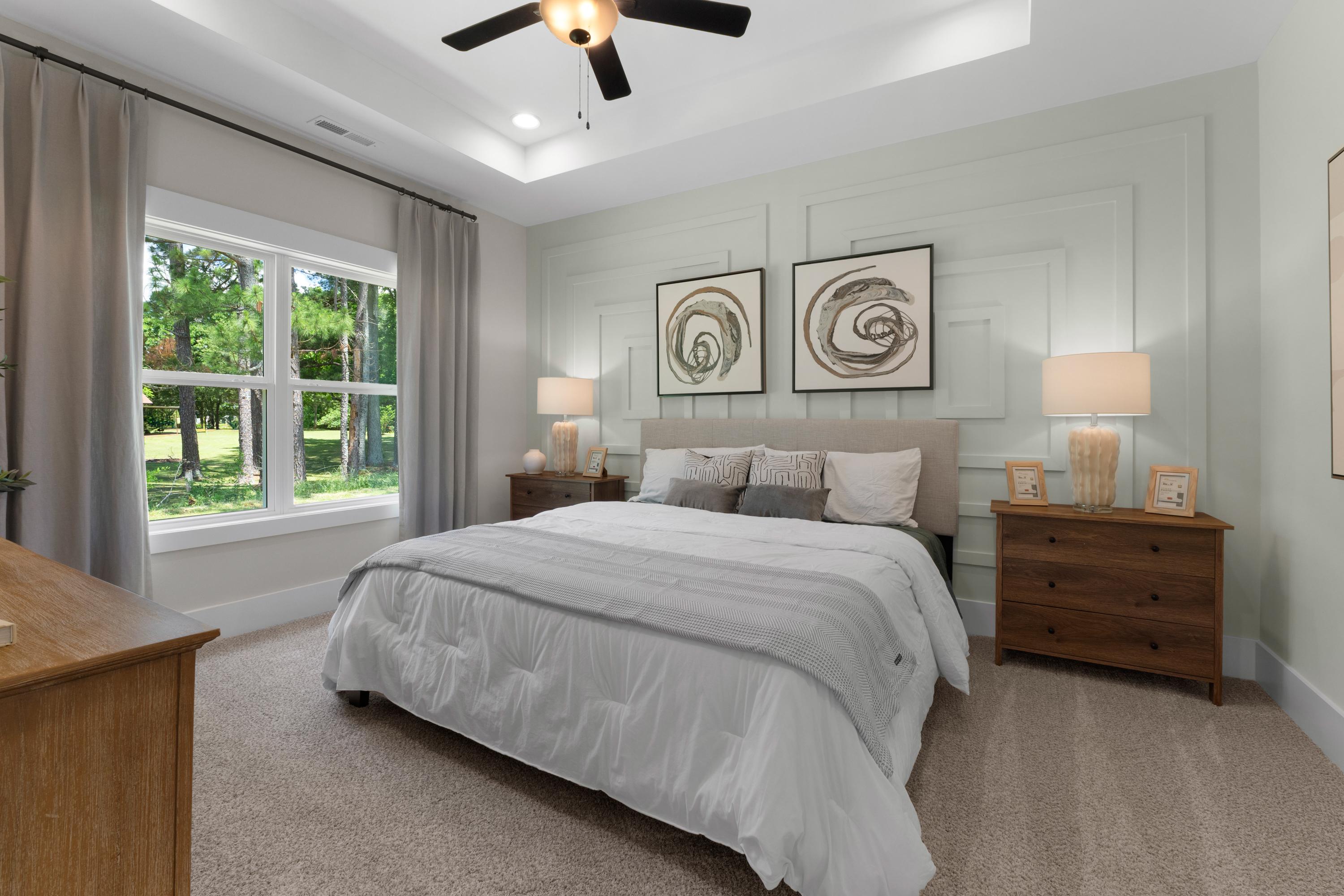 Spacious primary bedroom at Hollon Meadow in Decatur Alabama with king bed, neutral walls, abstract art, and tree-view windows