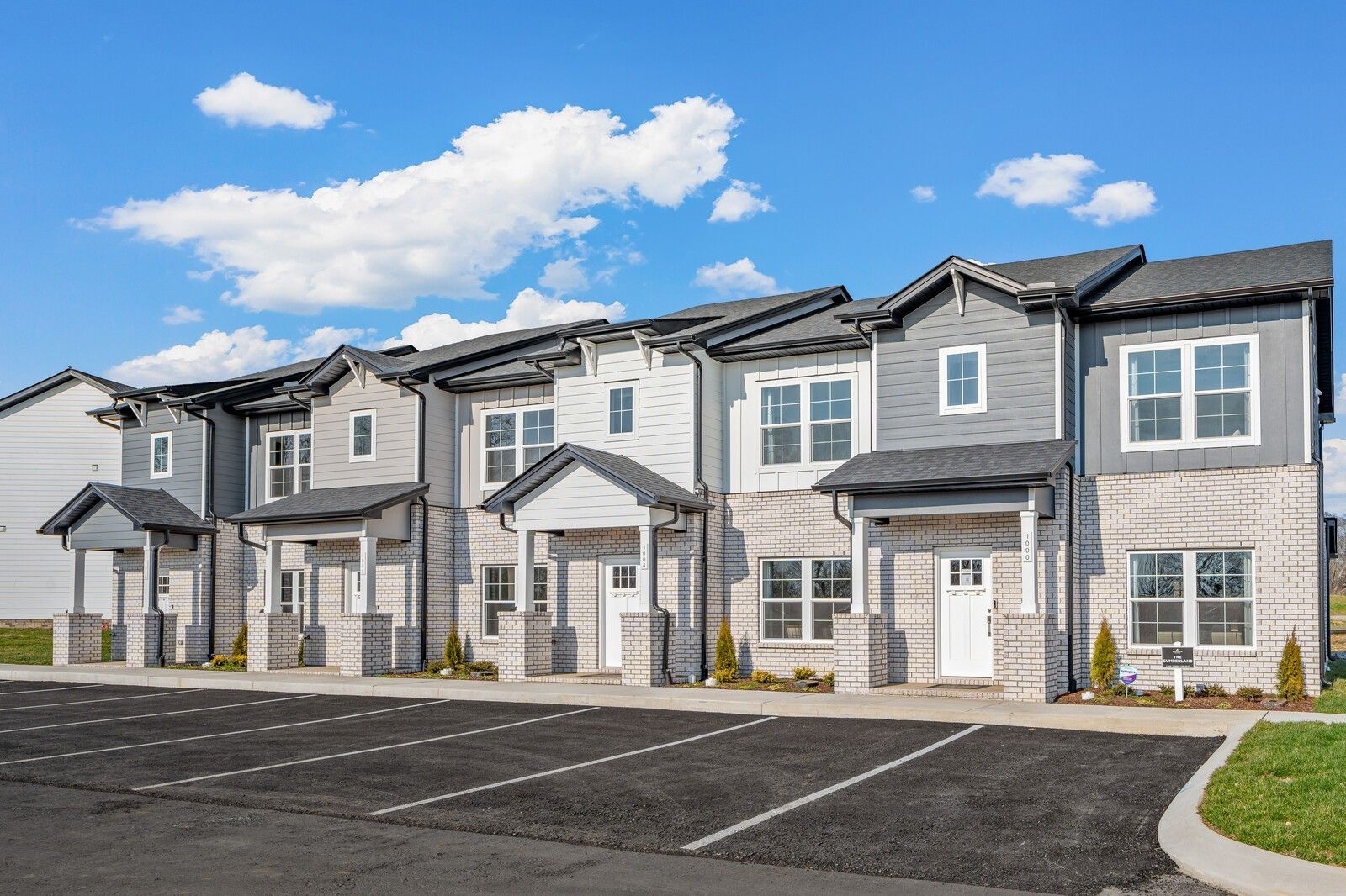 Row of modern 2-story townhomes with gray siding, brick accents, and covered porches in The Towns at Red River, Gallatin, Tennessee