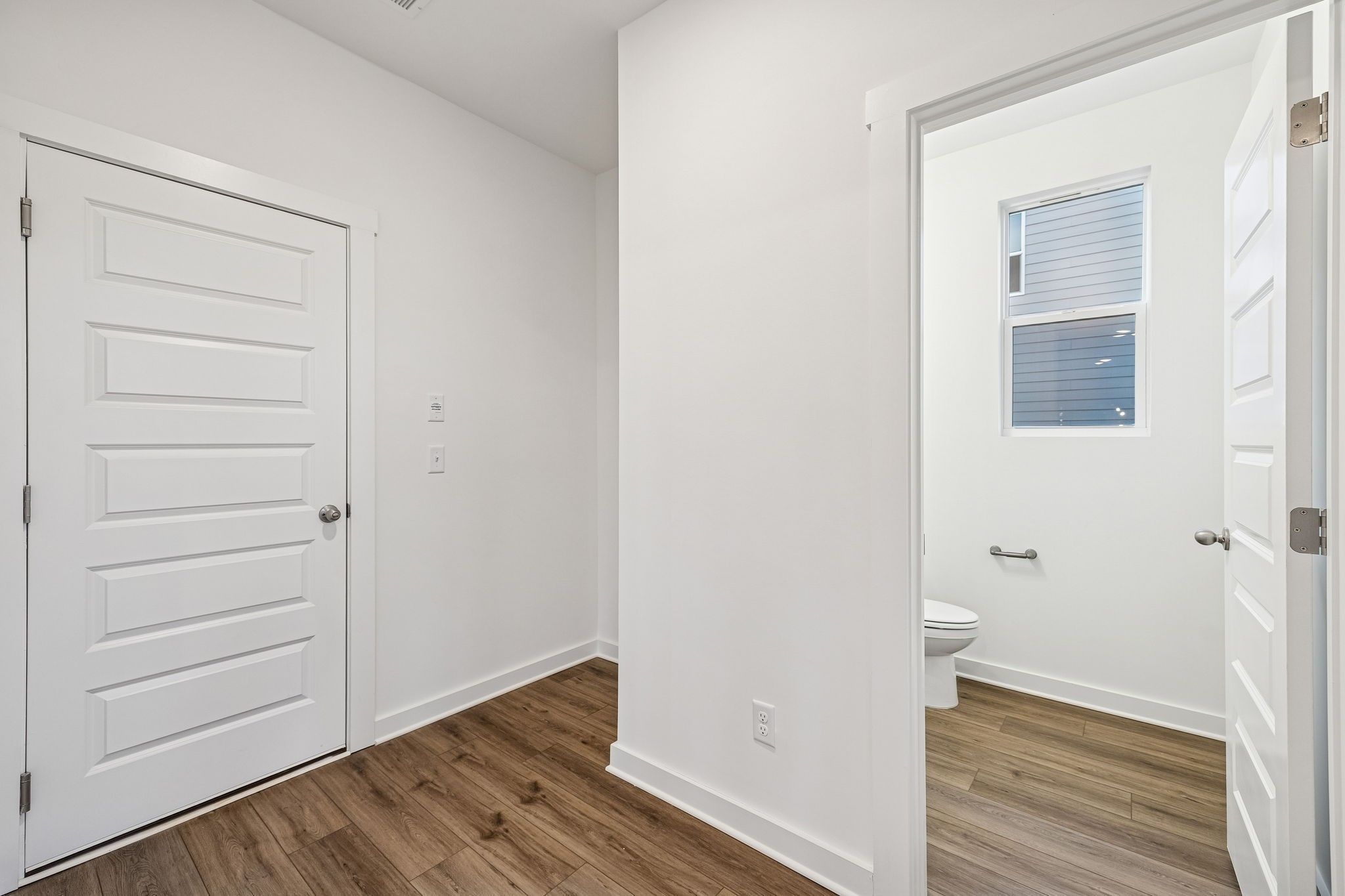 Bright half bath featuring white toilet, grab bar, frosted window, open door, and wood floors in Davidson Homes The Willow, White House TN