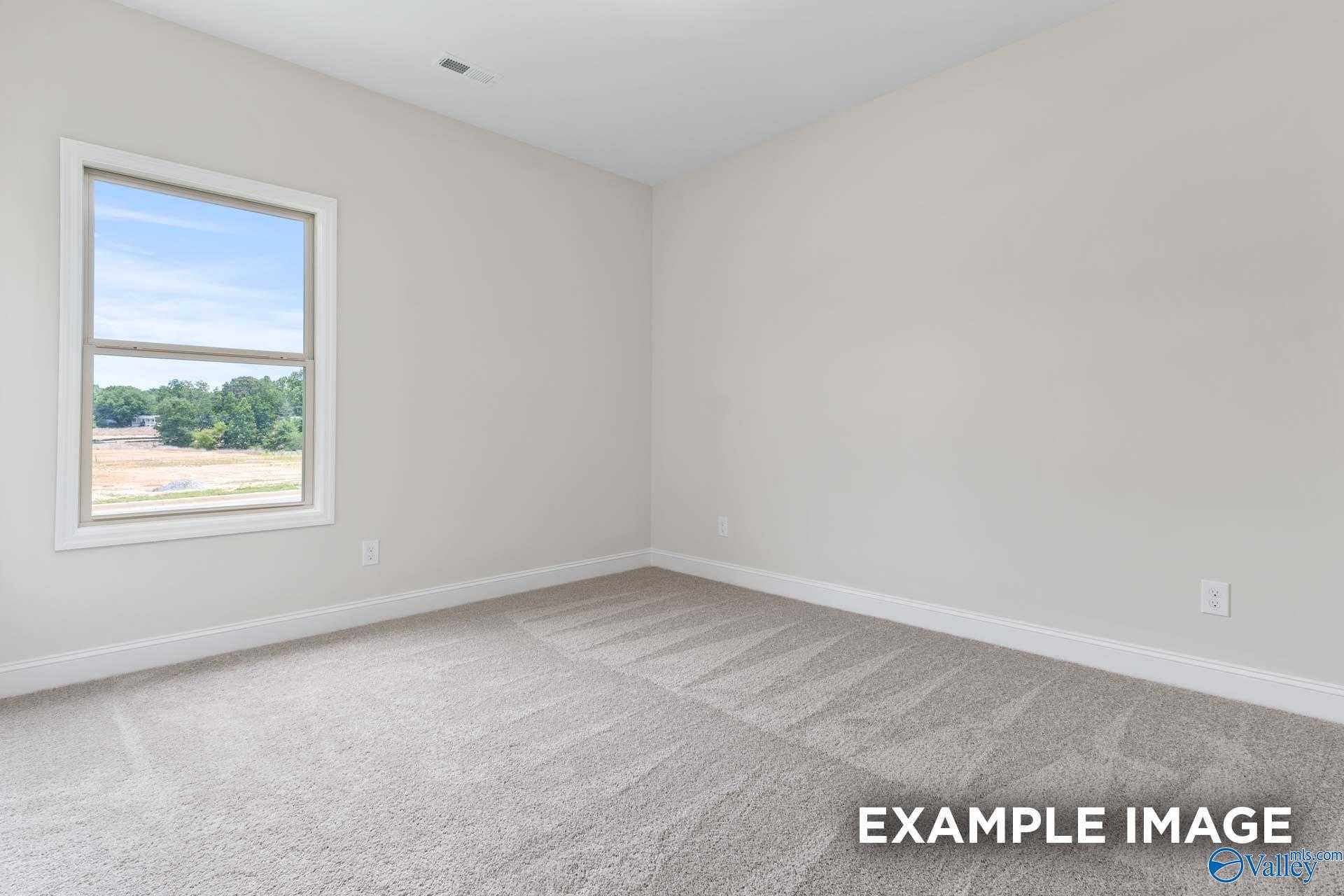 Bright secondary bedroom with neutral gray walls, carpeted floor, and large window view in 4-bedroom Daphne D home, Arab, Alabama