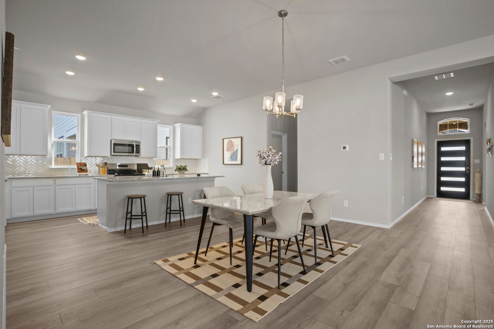Open-concept kitchen with white cabinets, island bar, and dining table under pendant lights in The Collin B home, Seguin, Texas