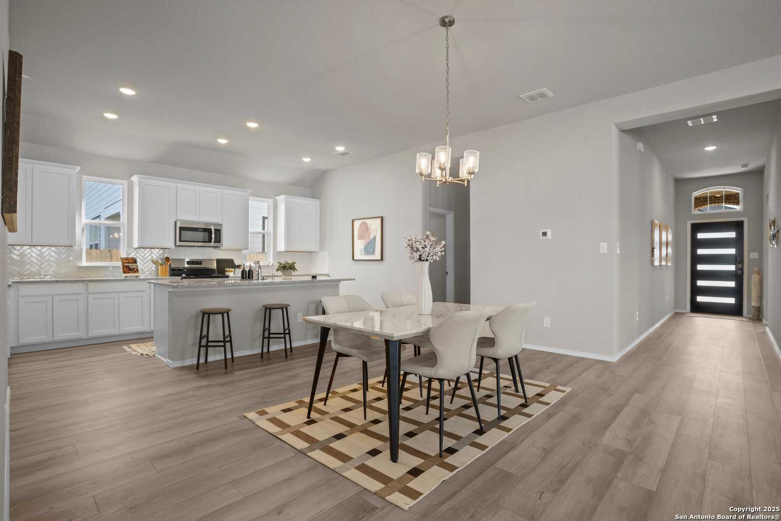 Open-concept kitchen with white cabinets, island bar, and dining table under pendant lights in The Collin B home, Seguin, Texas
