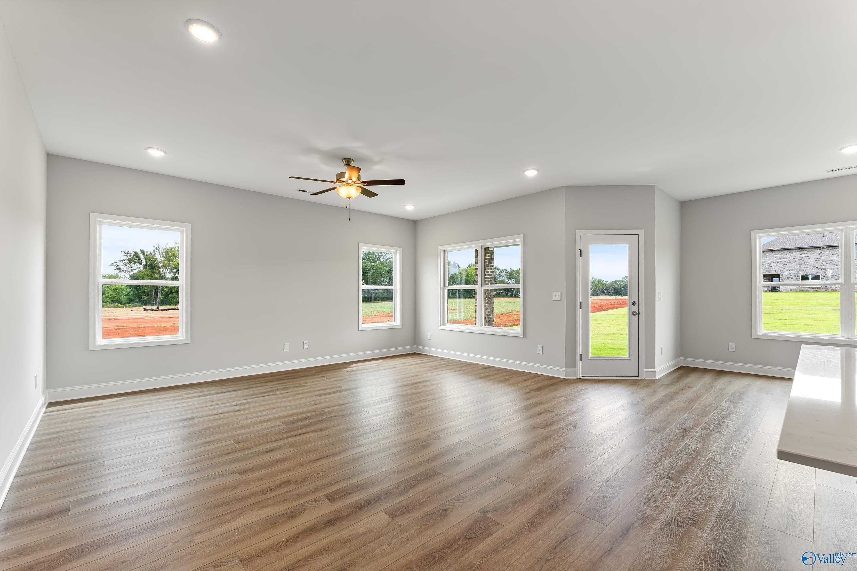 Bright open living room with hardwood floors, ceiling fan, and large windows to green yard in Davidson Homes The Franklin, Athens AL