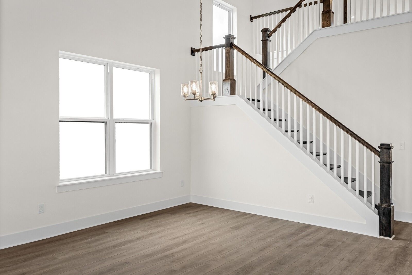 Elegant wooden staircase with chandelier, large windows, and hardwood floors in The Ridgeport D two-story home, Mt. Juliet, TN