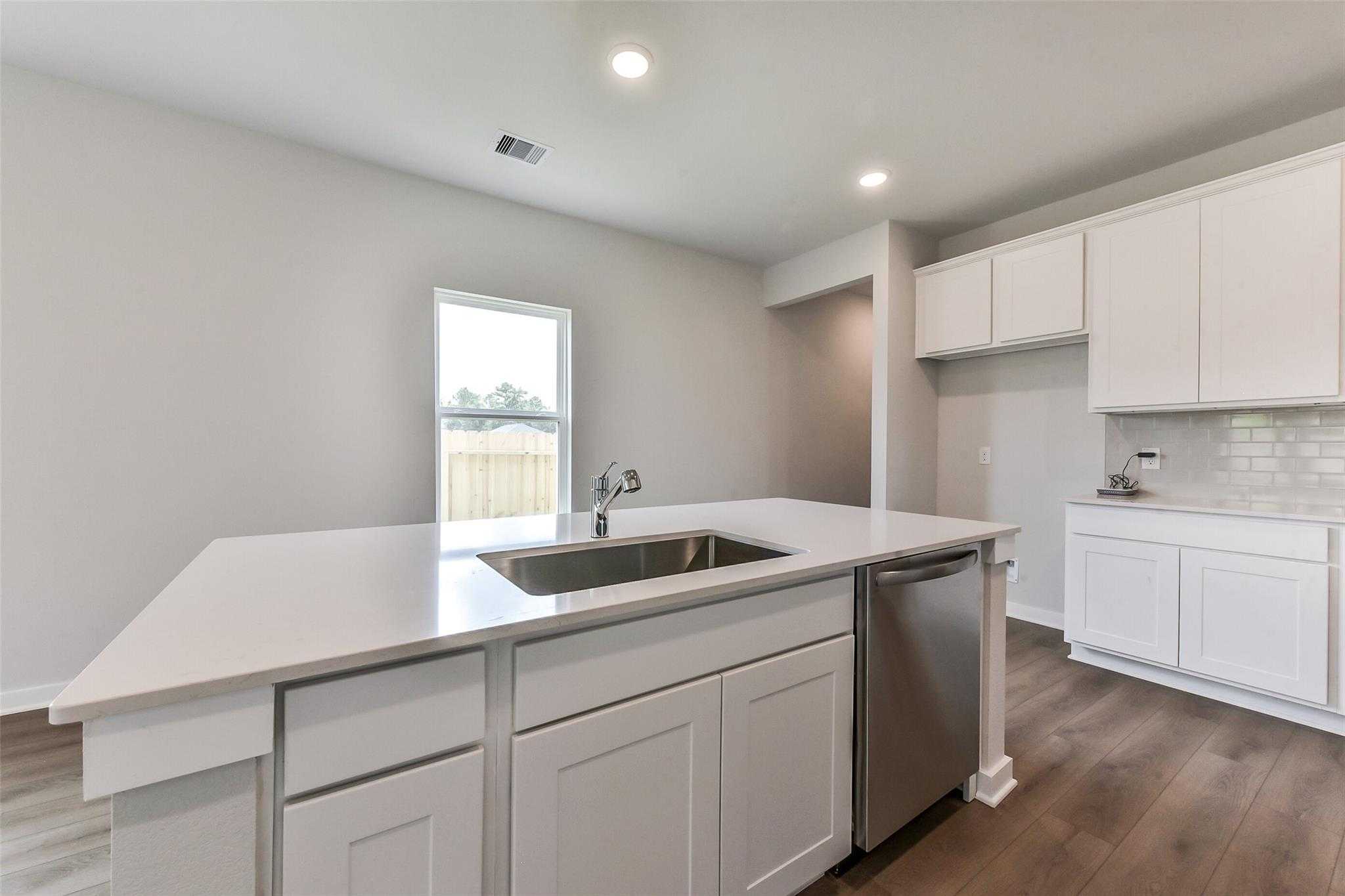 Modern white kitchen island with stainless sink, dishwasher, subway tile backsplash in Davidson Homes The Frio F, Dayton Texas