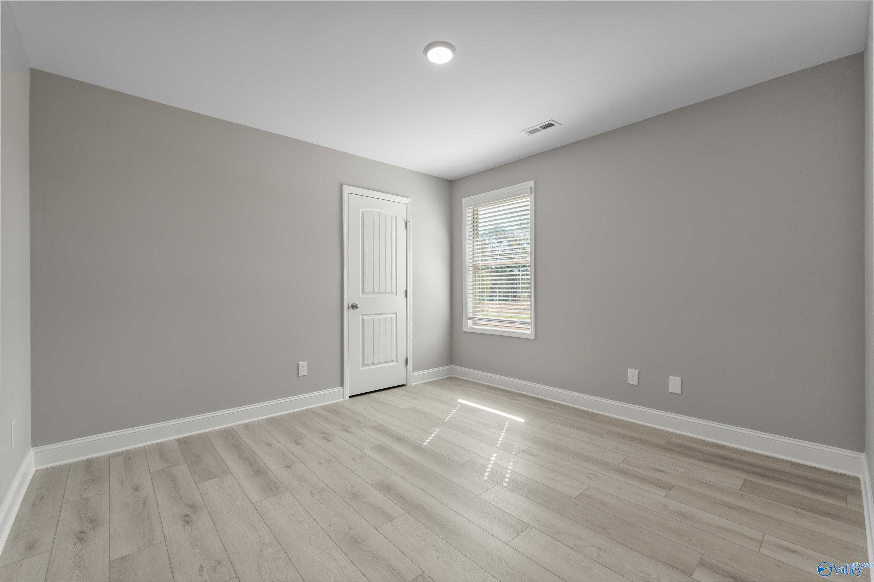 Bright secondary bedroom with gray walls, light hardwood floors, and window blinds in Davidson Homes The Everett B, Athens, Alabama