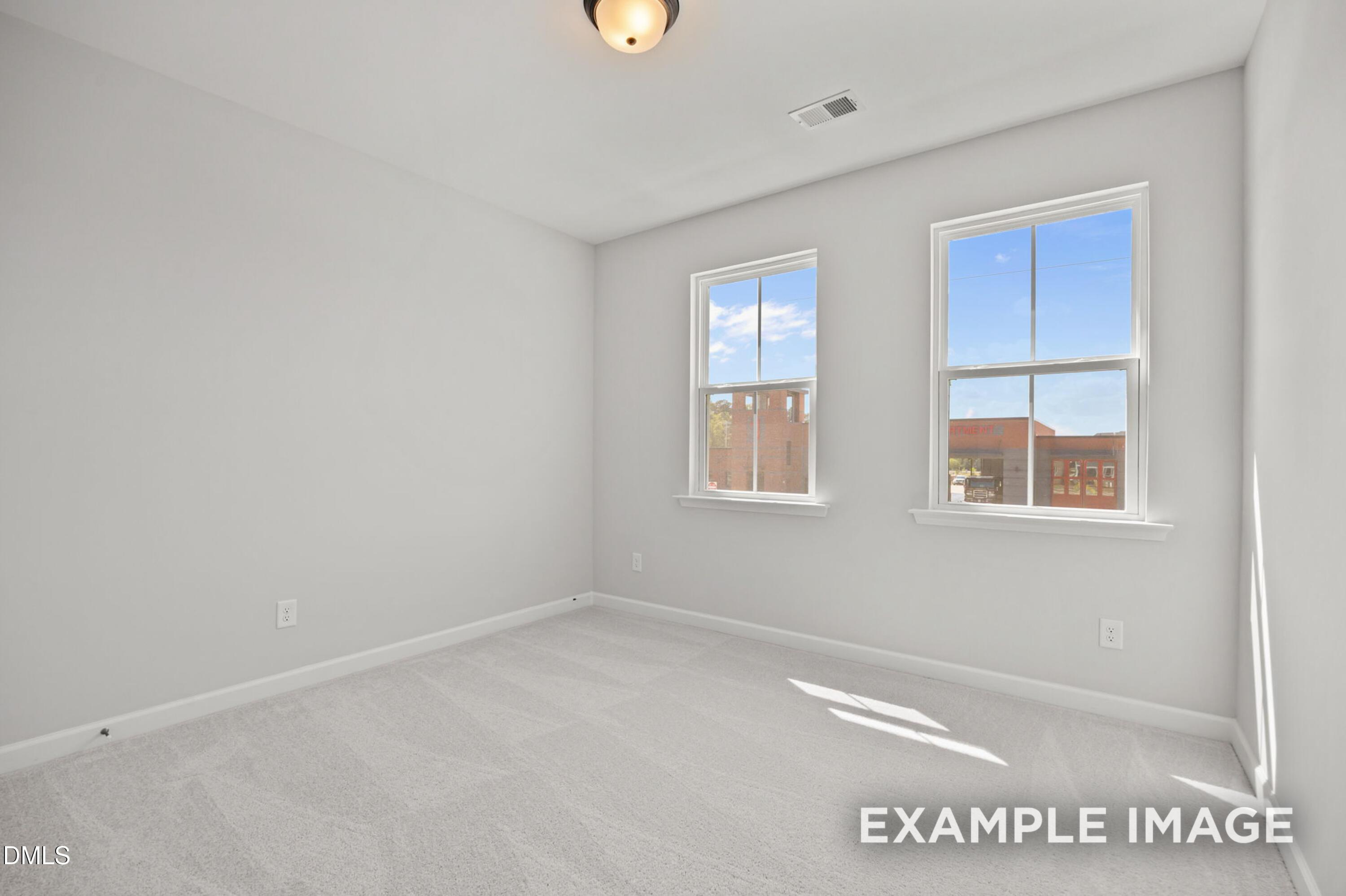 Bright bedroom with neutral carpet and two windows in The Alexander B floor plan by Davidson Homes in Knightdale, NC.