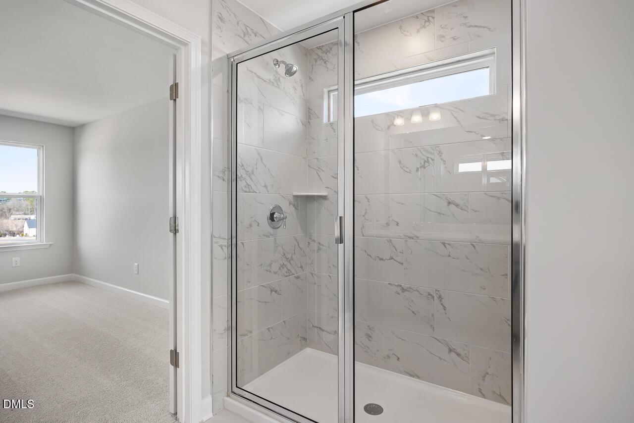 Elegant frameless glass shower with marble tiles, rainfall head, and window in master bath of Davidson Homes The Willow G, Angier, NC