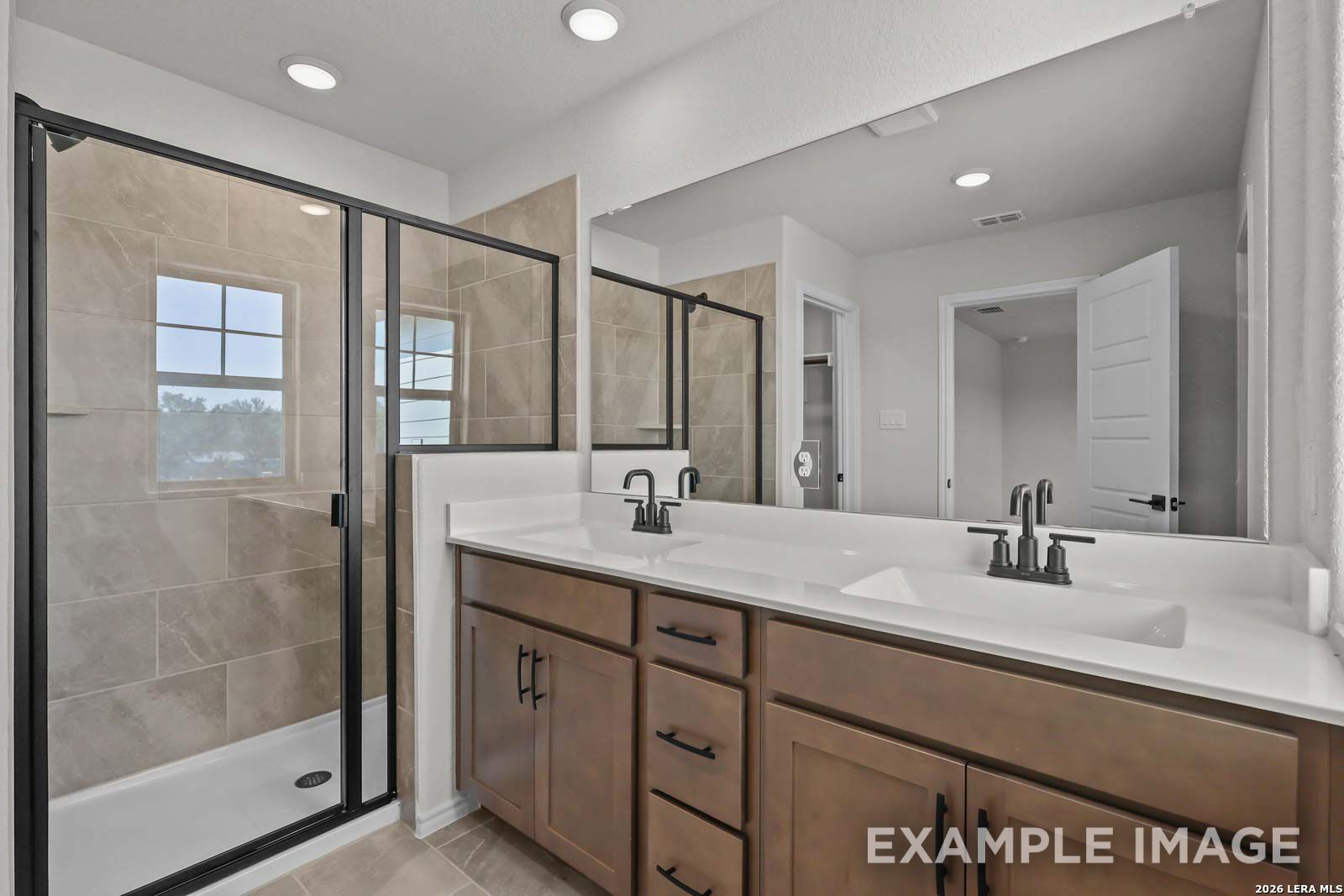 Modern bathroom with double vanity, walk-in tile shower, and dark fixtures in The Florence D at Cedar Heights, San Antonio.