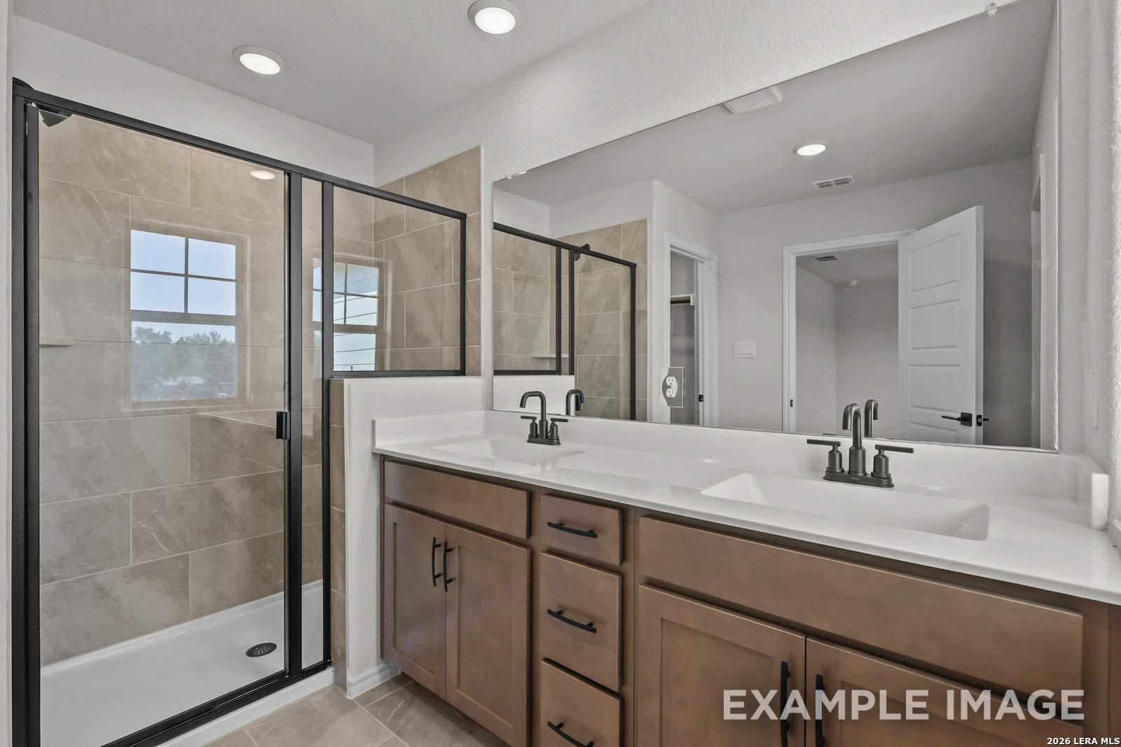 Modern bathroom with double vanity, walk-in tile shower, and dark fixtures in The Florence D at Cedar Heights, San Antonio.
