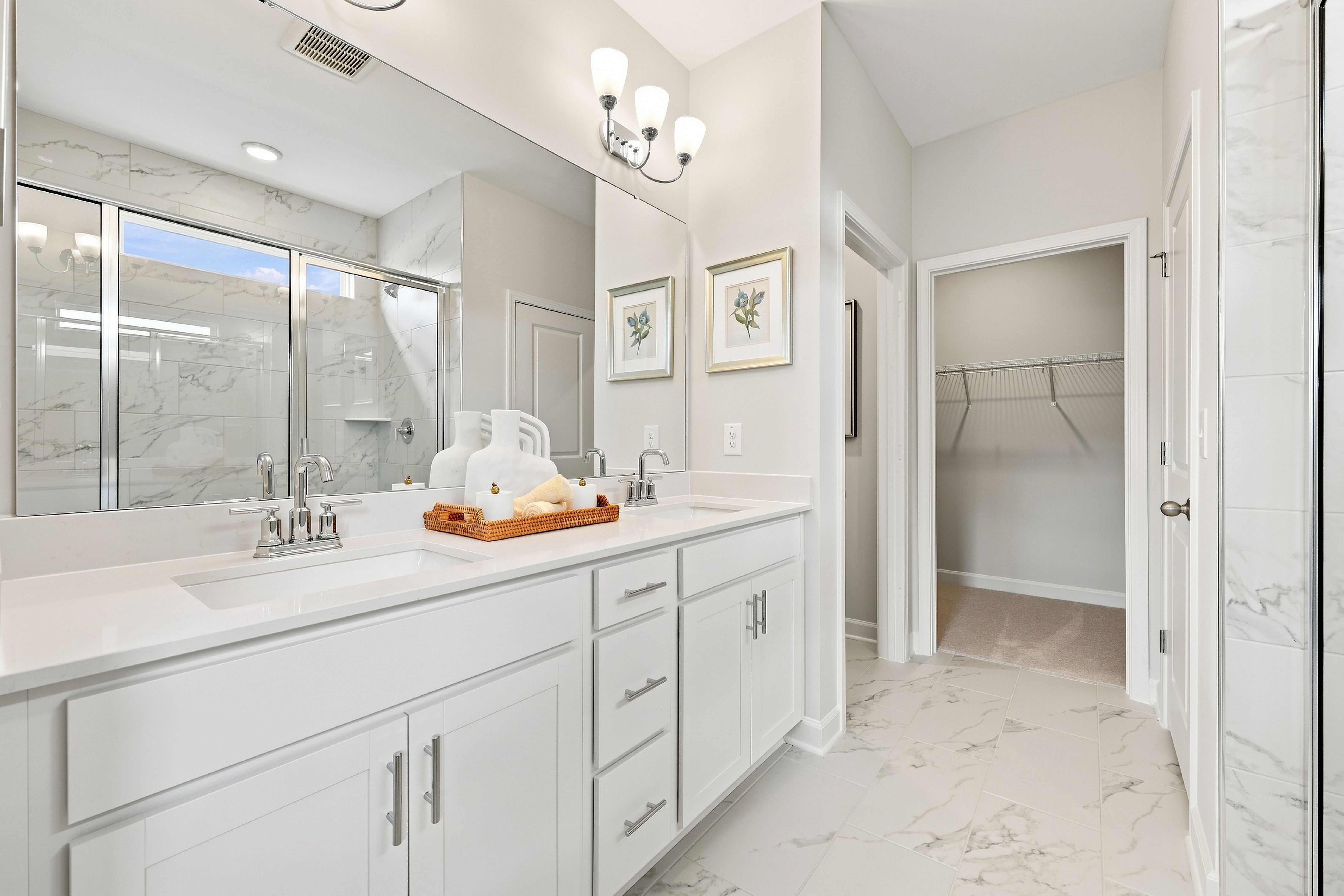 Modern master bathroom in The Daphne featuring a dual-sink white vanity, marble-style flooring, and walk-in closet access.