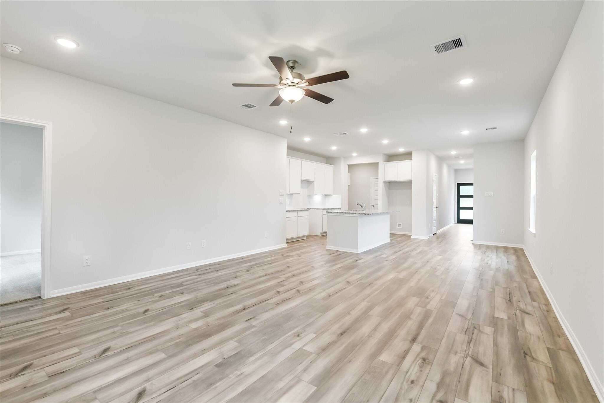 Spacious open living area with kitchen island, white cabinets, ceiling fan, and light hardwood floors in The Brazos F home, Conroe, Texas