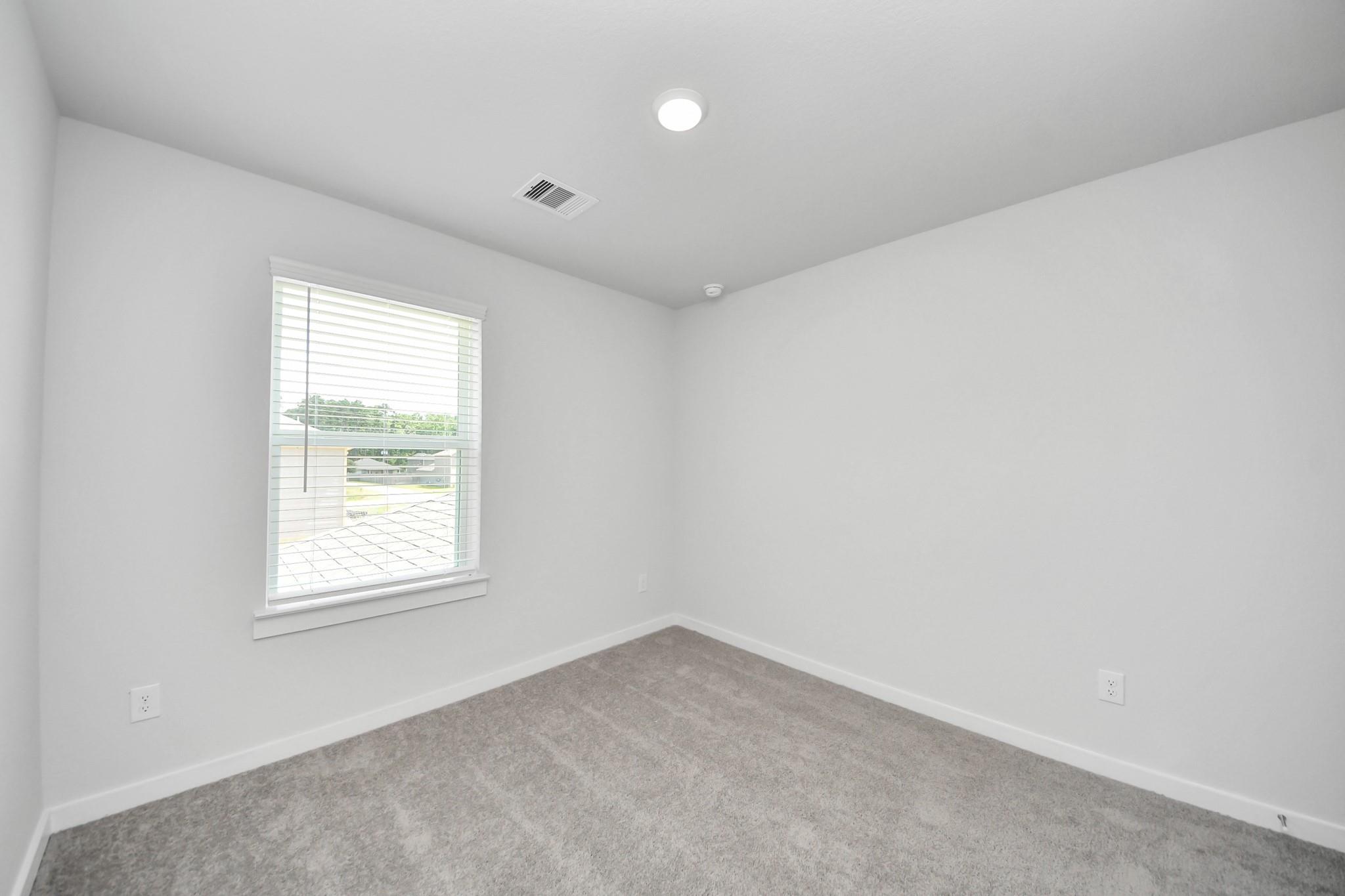 Bright, carpeted bedroom with white walls and natural light in The Brazos F floor plan at Liberty Estates, Cleveland, TX.