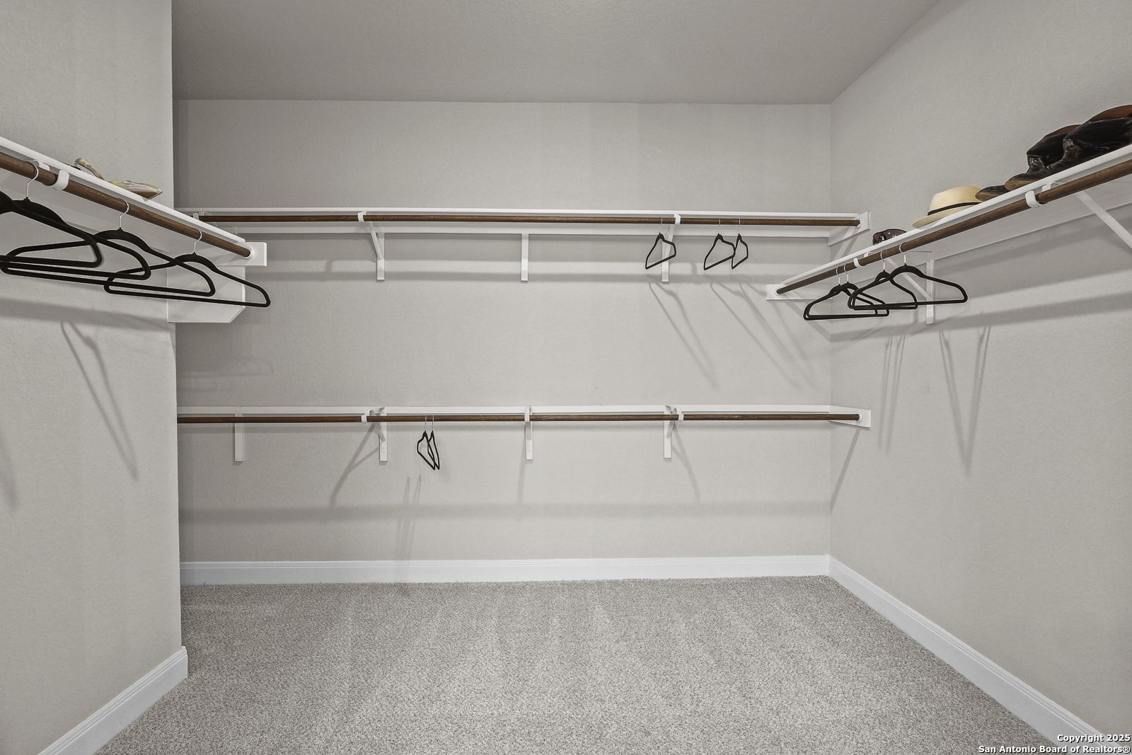 Spacious walk-in closet with white shelves, hanging rods, hats, and shoes in Davidson Homes The Jennings G, Castroville, Texas