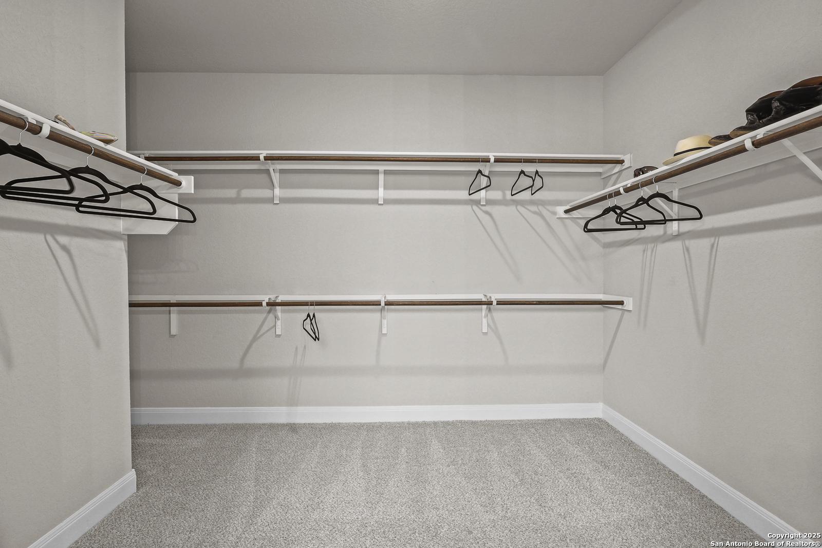Spacious walk-in closet with white shelves, hanging rods, hats, and shoes in Davidson Homes The Jennings G, Castroville, Texas